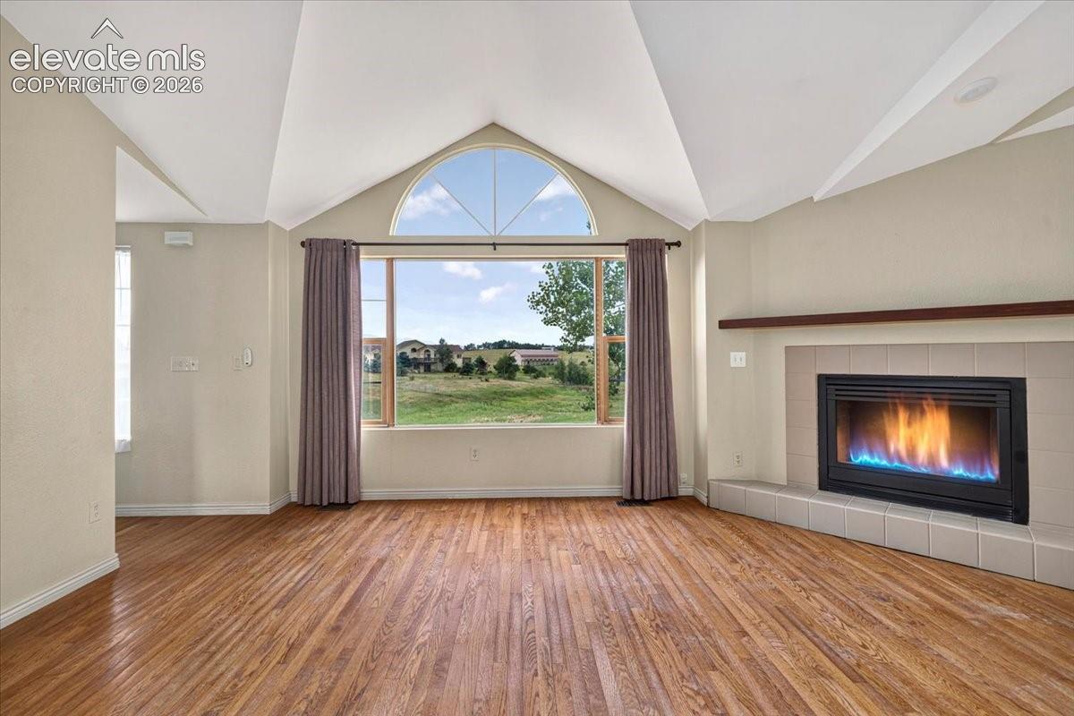 Vaulted ceiling featuring an arched window, wood-finish flooring, and a fireplace with a tile surround and wood mantel