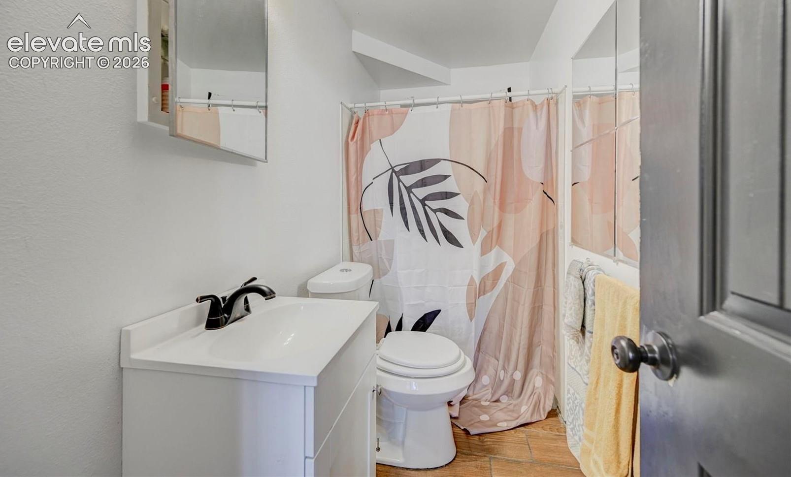 Bathroom featuring wood-finish flooring, a white vanity cabinet with a integrated sink, matte black faucet hardware, and a mirrored medicine cabinet