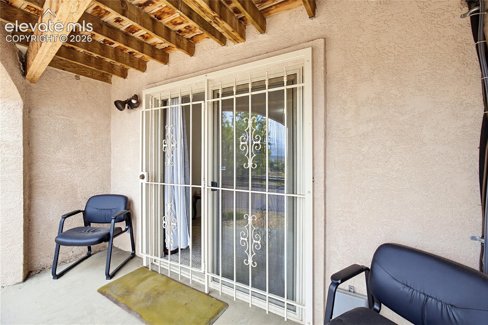 Covered patio featuring a wood-beam ceiling, stucco wall finish, and sliding glass door with security bars