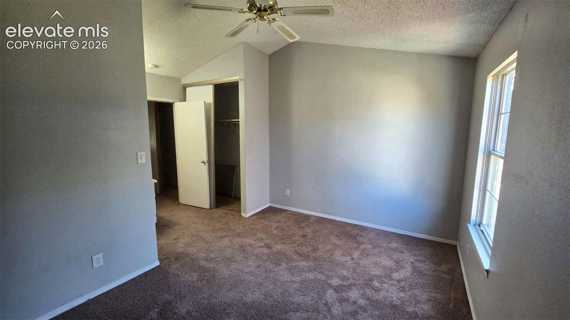 Vaulted ceiling featuring a central lighted ceiling fan, neutral carpeting, and a built-in closet with sliding doors