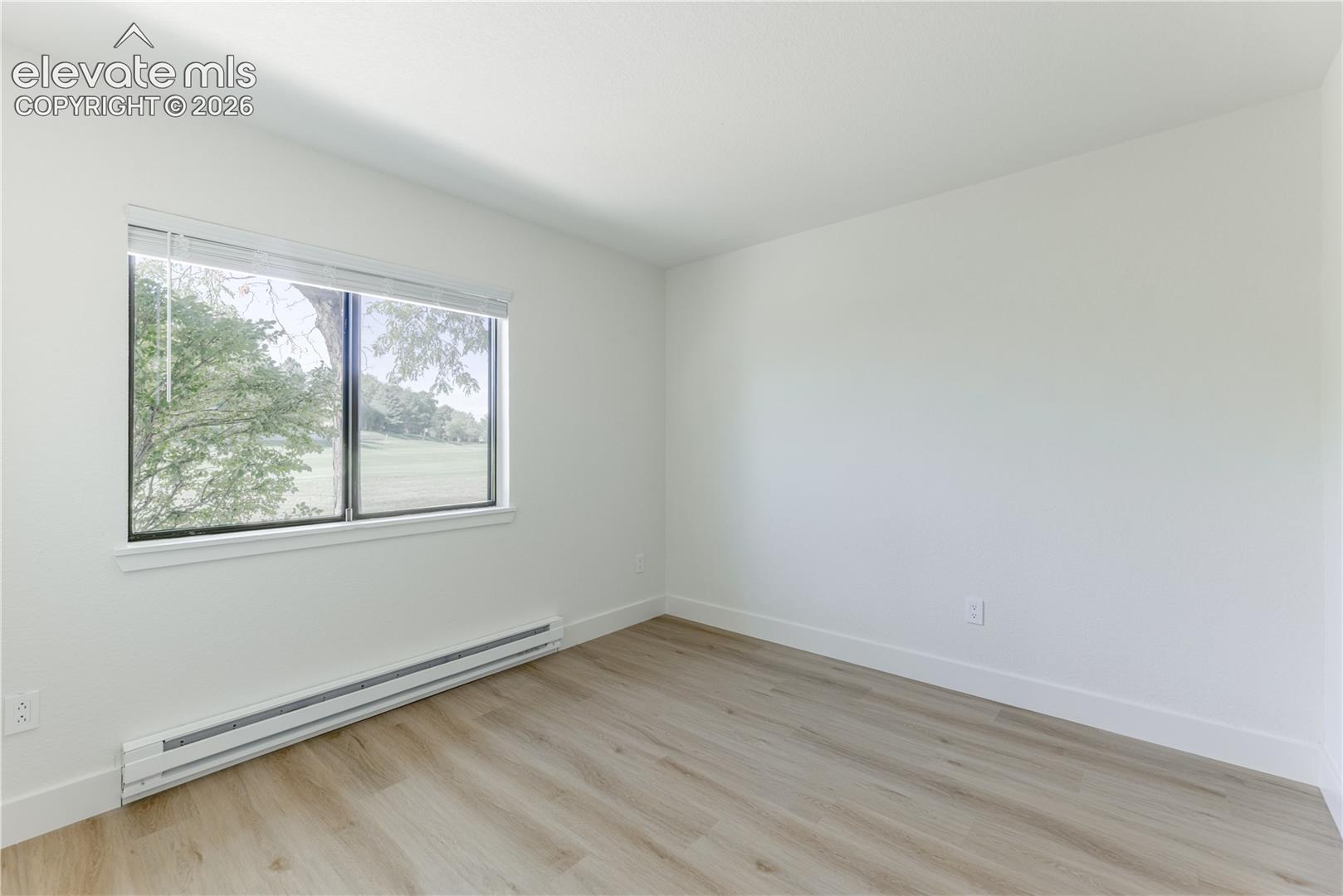 Neutral-toned wood-finish flooring, crisp white walls, and a large horizontal window providing natural light and exterior scenery