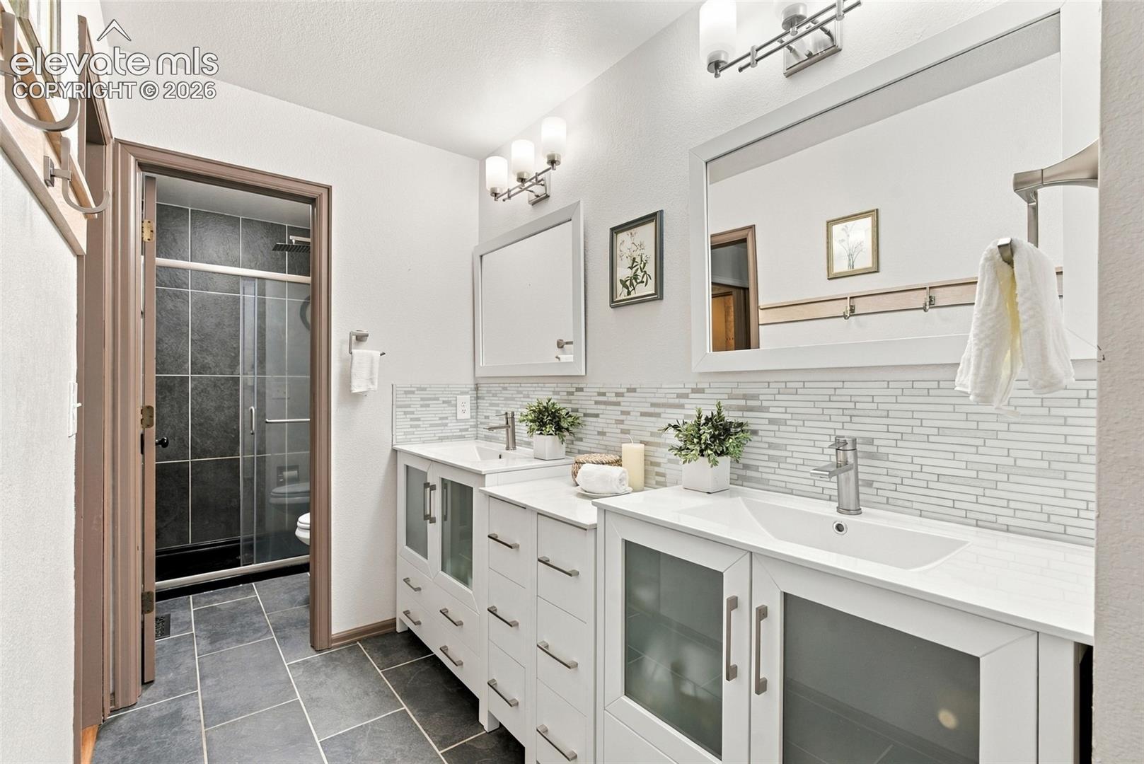 Primary Bathroom Dual white vanities with integrated sinks, contemporary wall-mounted lighting, and a linear tile backsplash