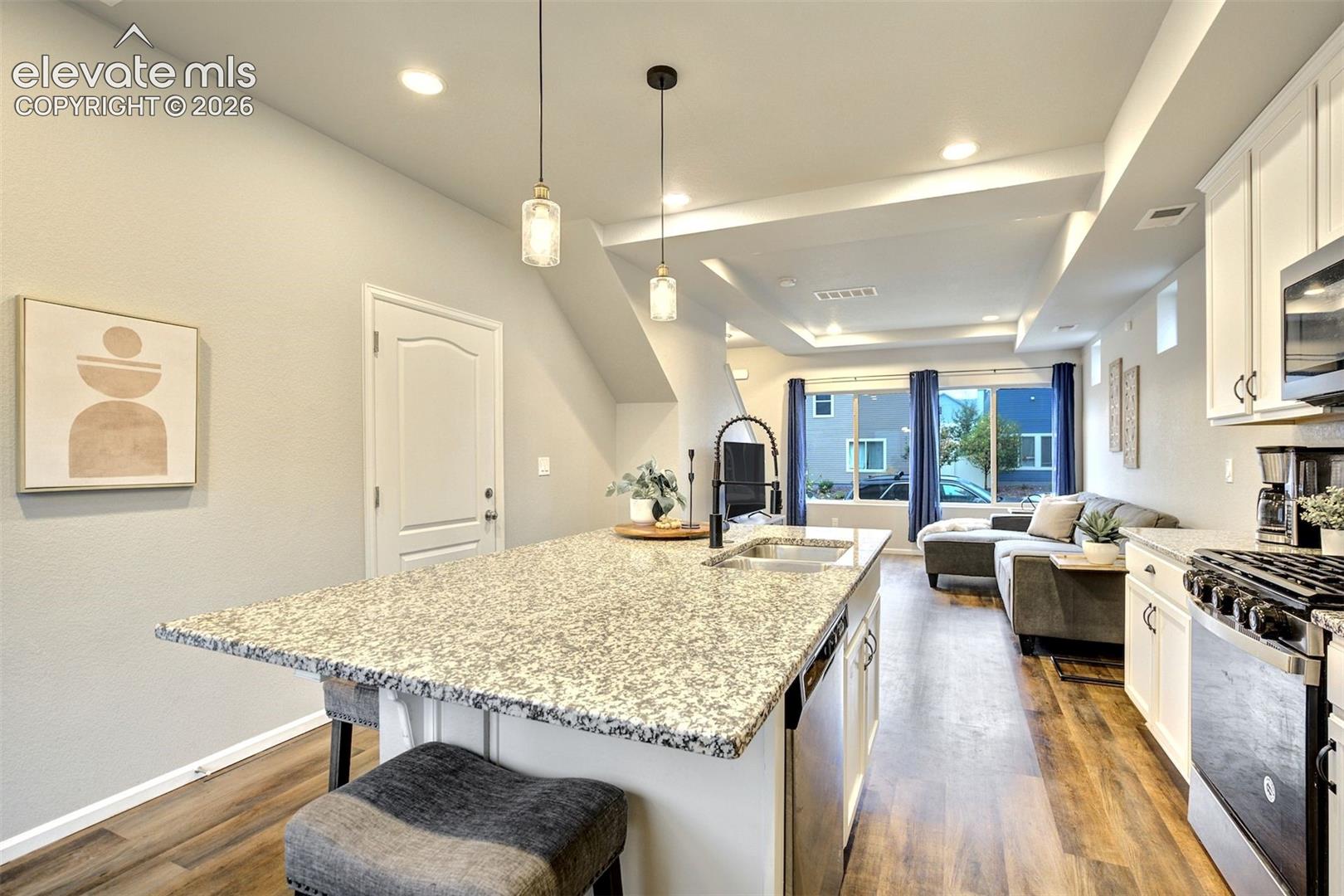 Kitchen featuring an expansive stone-topped island with a dual-basin sink, modern pendant lighting, white cabinetry, and wood-finish flooring