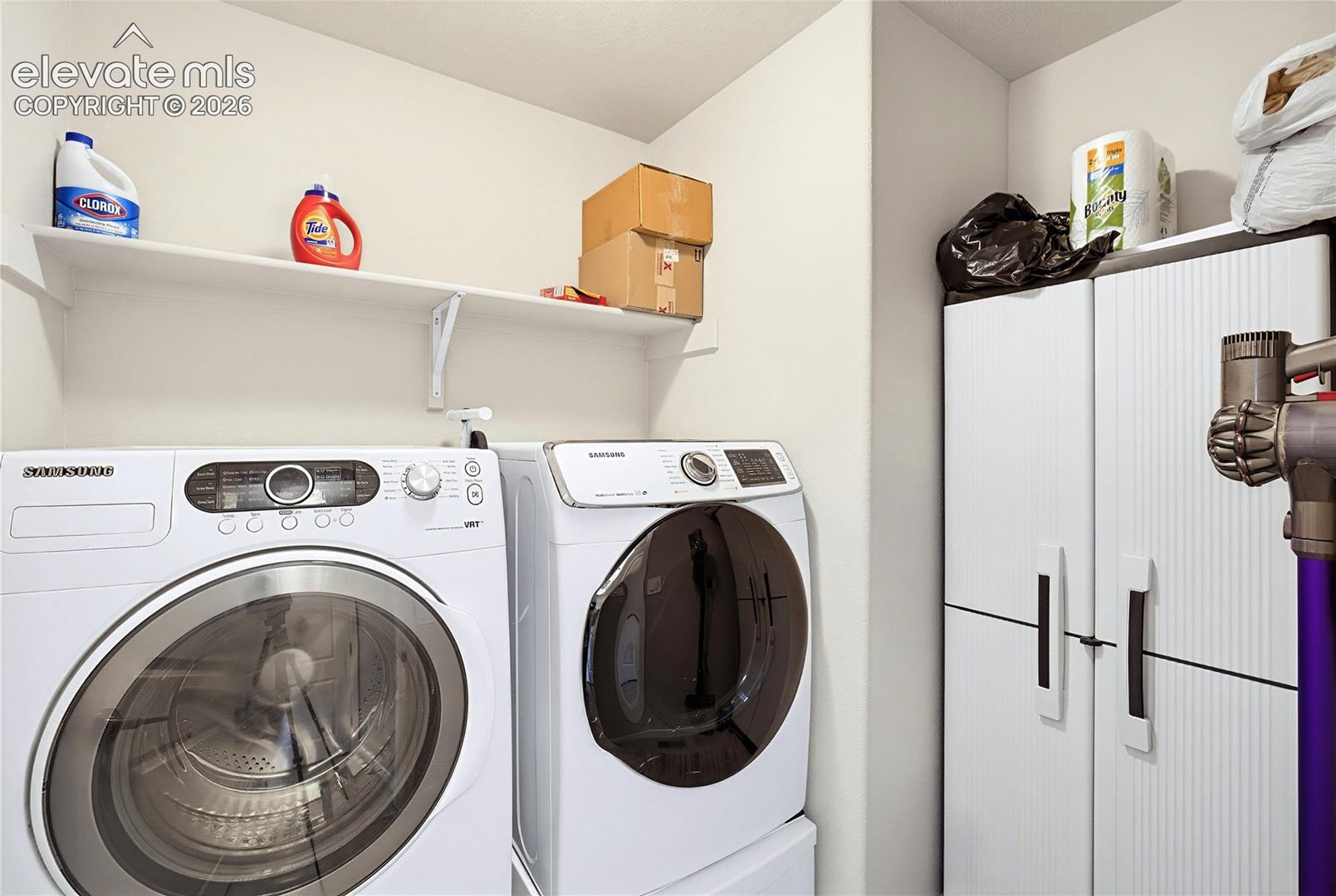 Laundry area featuring wall-mounted shelving and a tall storage cabinet with vertical-groove detailing