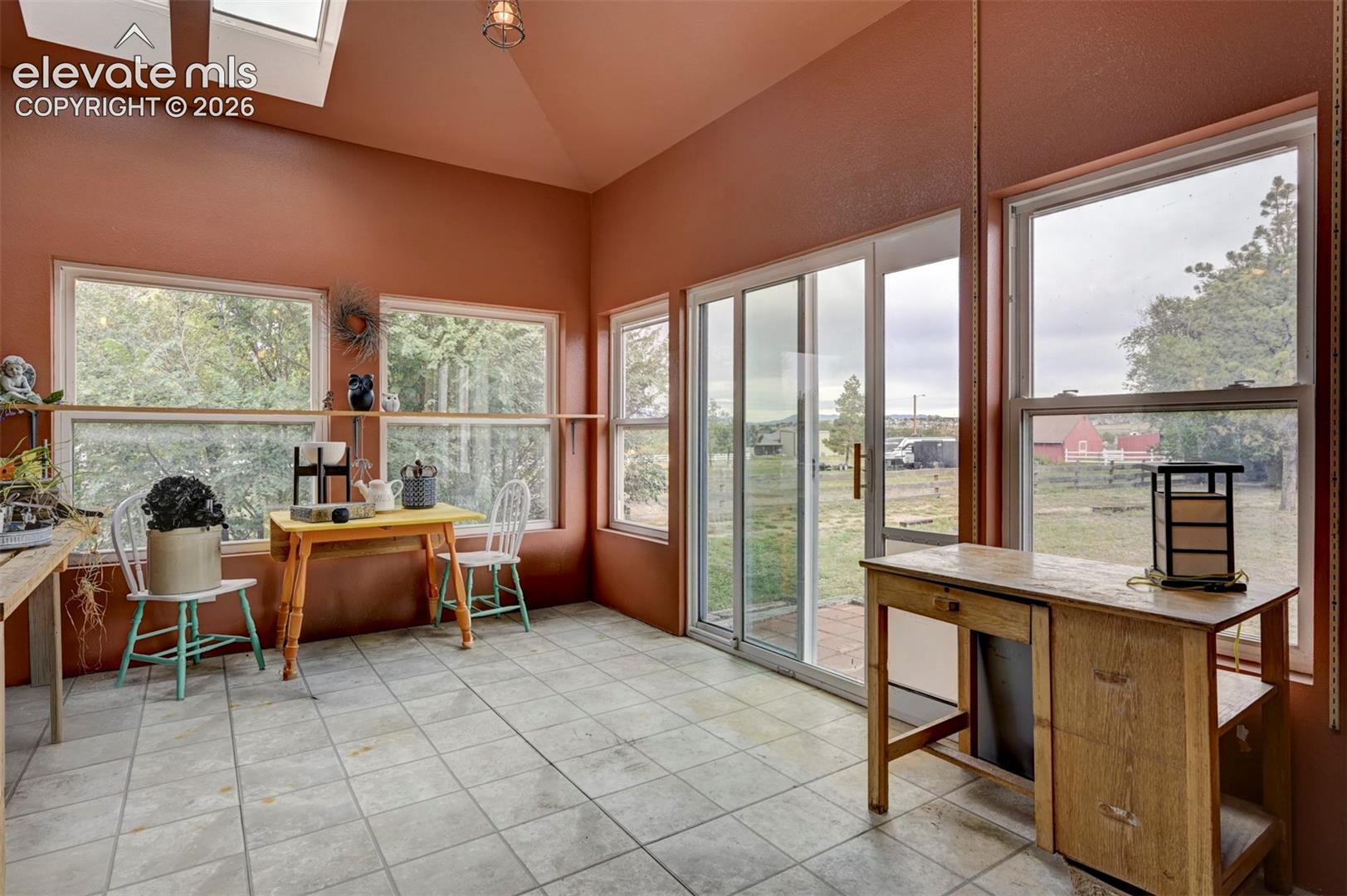 Vaulted ceiling with skylights, extensive window placement, sliding glass door access, and tile flooring