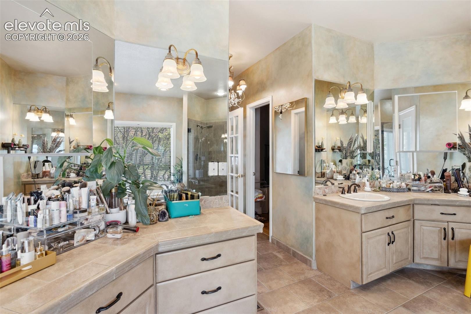 Spacious bathroom featuring double vanity with integrated sink, ample counter space, extensive mirror coverage, wall-mounted light fixtures, and a large window