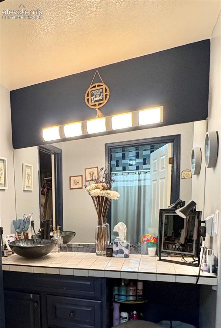 Custom vanity with a vessel sink, tile countertop, and integrated storage