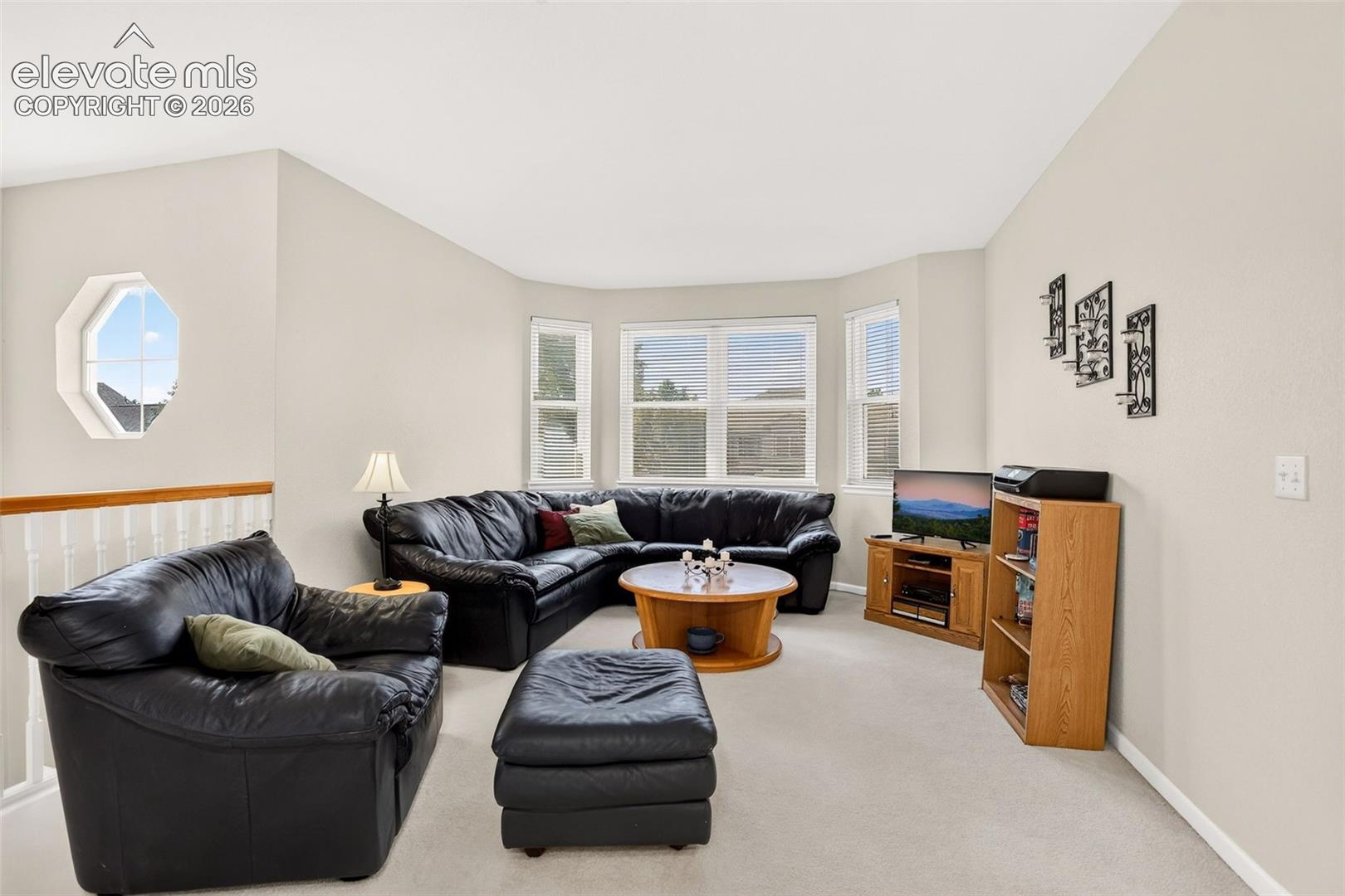 Vaulted ceiling, bay window, octagon window, light-colored carpeting, and a white railing with a wood-finish top