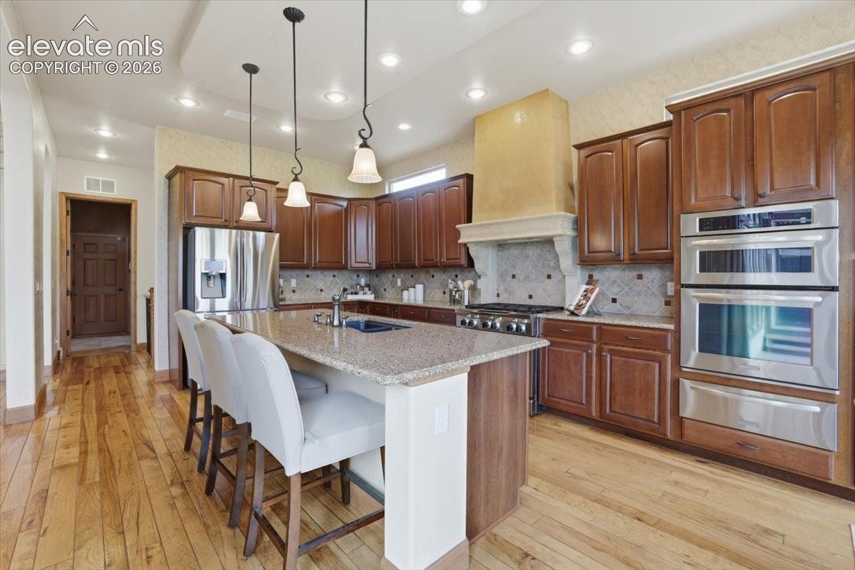 Gourmet Kitchen with Wood Flooring, Island, Granite Countertops, Deco Tile Backsplash, Hood Vent wrapped in Italian Plaster! Stainless Steel Appliances include a Dishwasher, Two Dishwasher Drawers, French Door Fridge, Warming Drawer, Built-in Oven, Built-in Microwave, and a 6-burner Gas Range atop a Second Oven.