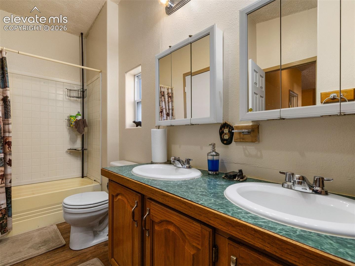 Bathroom featuring dual vanity with wood-finish cabinetry, countertop with integrated dual sinks, chrome-finish faucets, and mirrored medicine cabinets