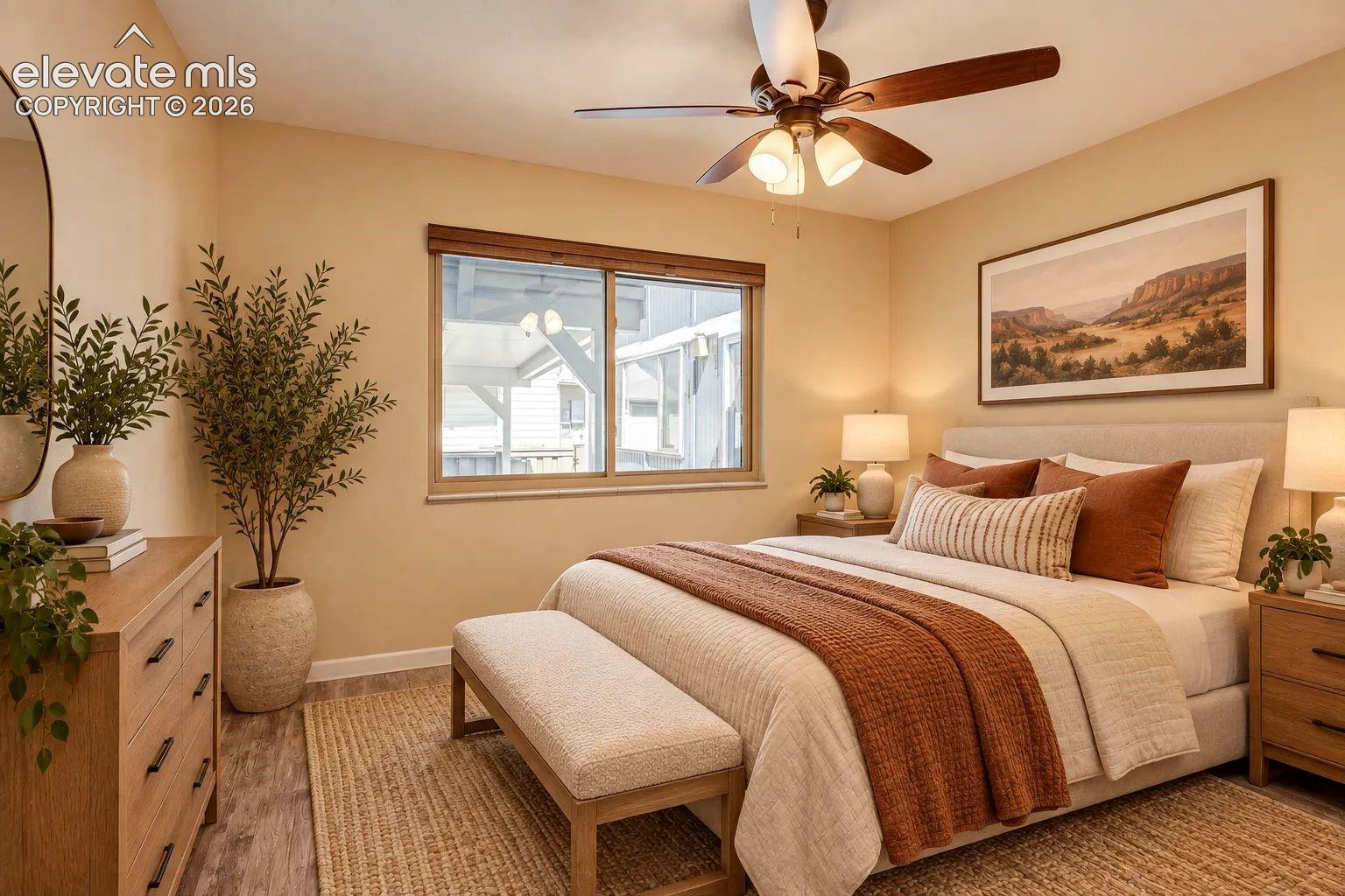 Bedroom featuring wood-finish flooring, a ceiling fan with integrated lighting, and a large window with wood-trim framing. AI-Enhanced – furniture/decor digitally added