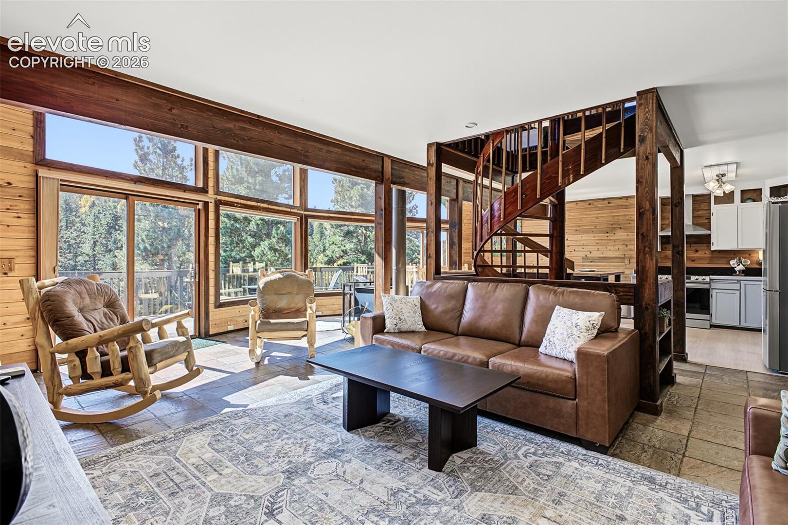 Expansive windows, wood-finish walls, spiral staircase, tile flooring, and integrated kitchen