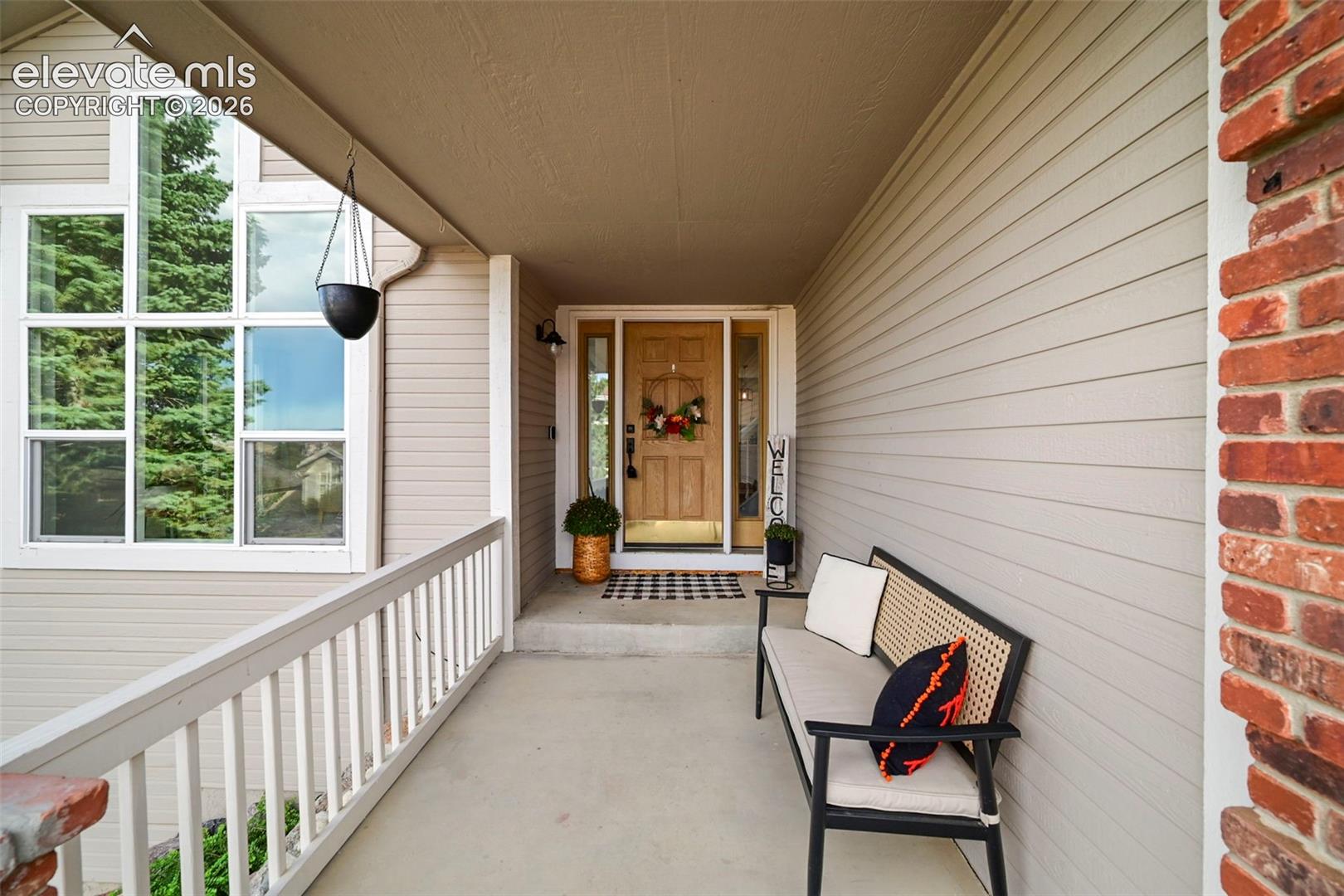 Covered front porch featuring a wood entry door, brick exterior accents, and horizontal siding