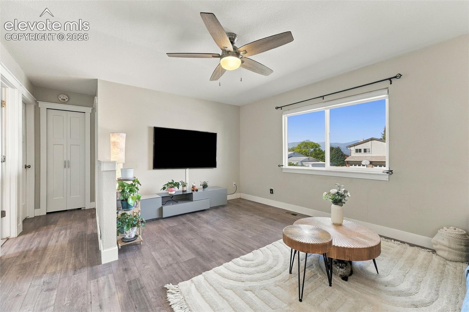 Wood-finish flooring throughout, ceiling fan with integrated lighting, window with mountain backdrop, and bi-fold closet doors
