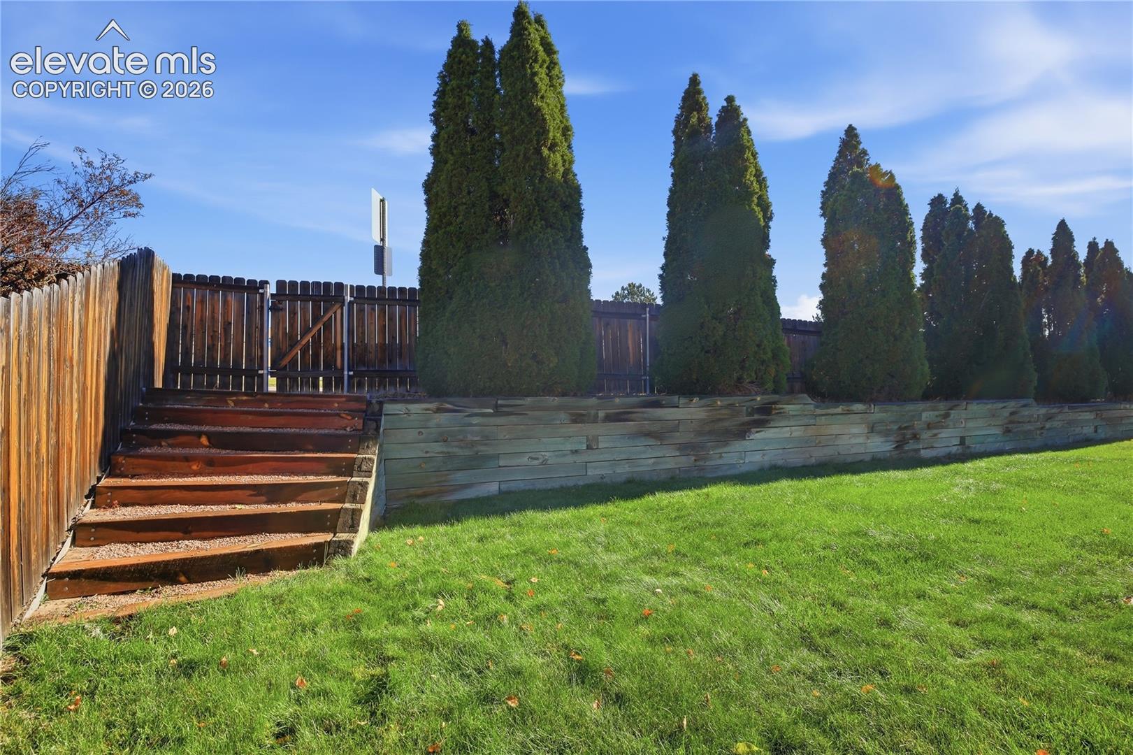 BACKYARD FEATURING A TIERED LAWN, WOOD RETAINING WALL, CUSTOM TIMBER STAIRS, AND A WOODEN PRIVACY FENCE ACCENTED BY MATURE EVERGREEN TREES