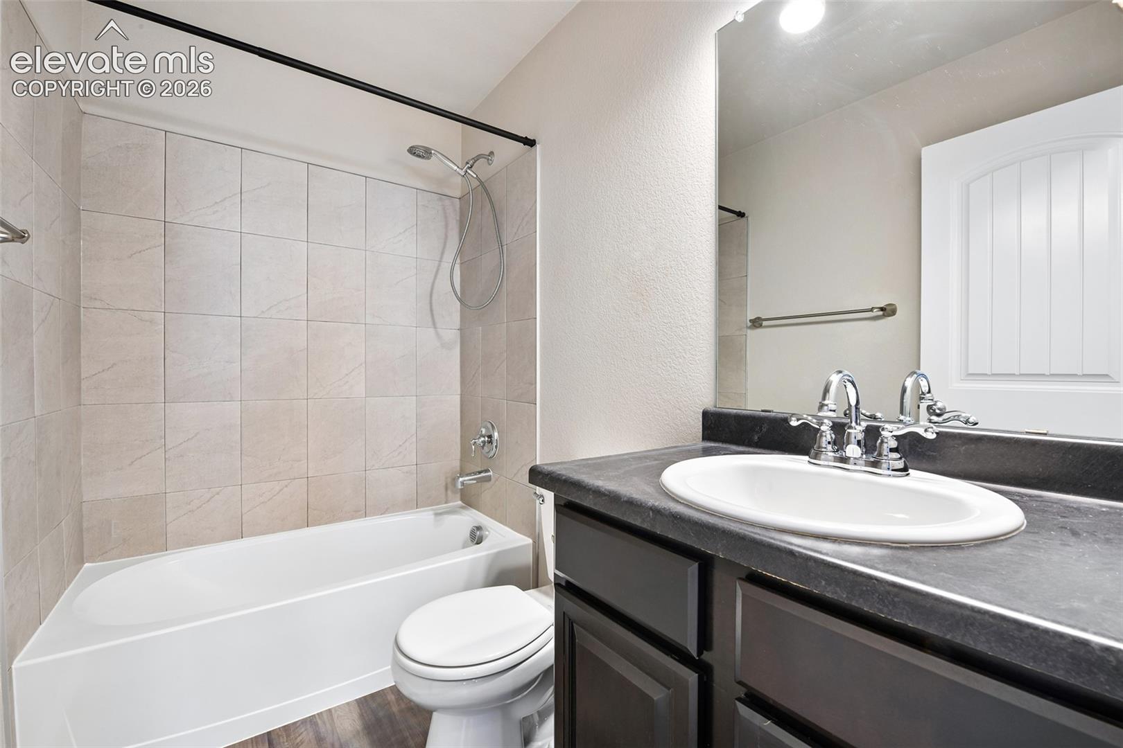 Bathroom featuring a single-sink vanity with dark cabinetry and a solid-surface countertop, a bathtub and shower combination with full-height tile surround, and a wall-mounted vanity mirror