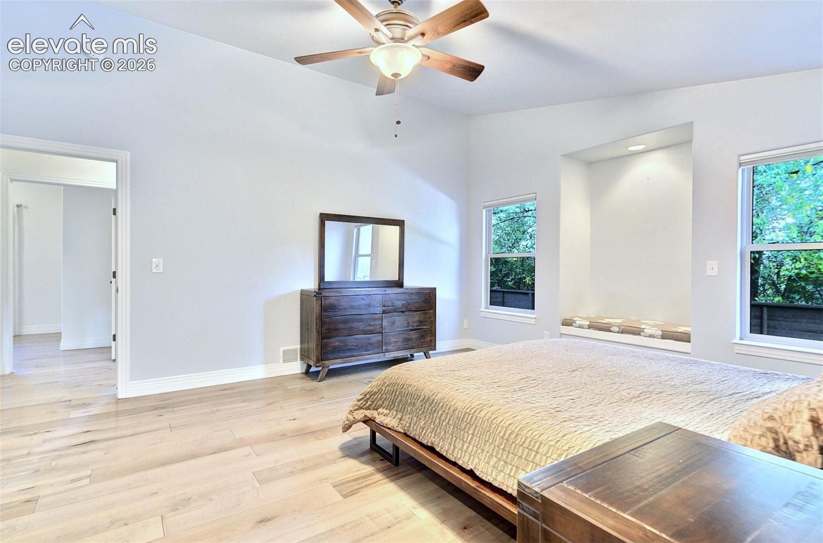 Vaulted ceilings, wood-finish flooring, recessed architectural alcove with built-in seating, and a multi-blade ceiling fan with integrated lighting