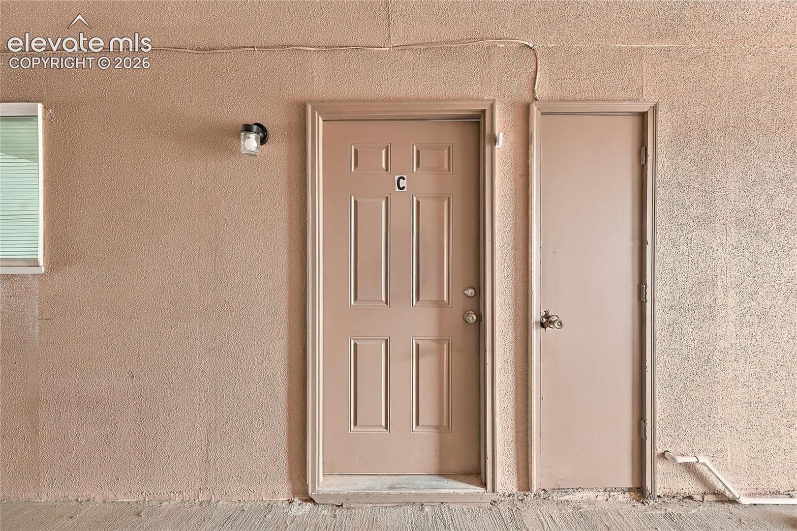 Entry featuring a six-panel door with metal hardware and an attached exterior wall-mounted light fixture