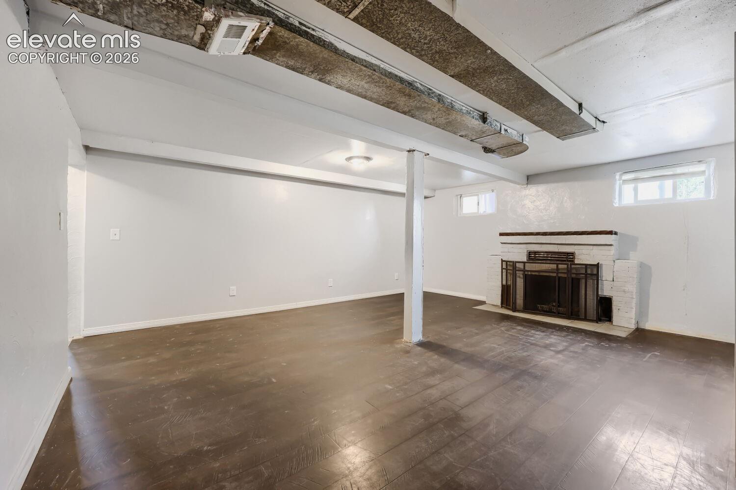 Spacious room with dark wood-finish flooring, a white brick fireplace, and overhead lighting