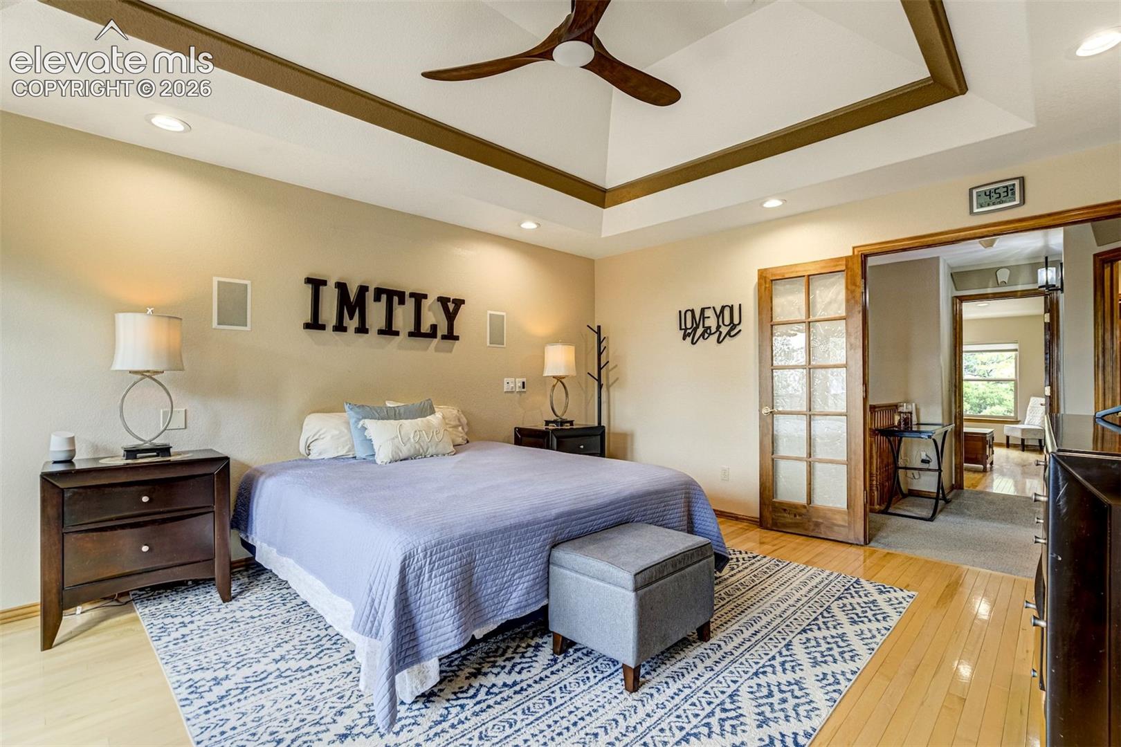 Tray ceiling with recessed lighting and a ceiling fan, light wood-finish flooring, and French doors leading to an adjoining room