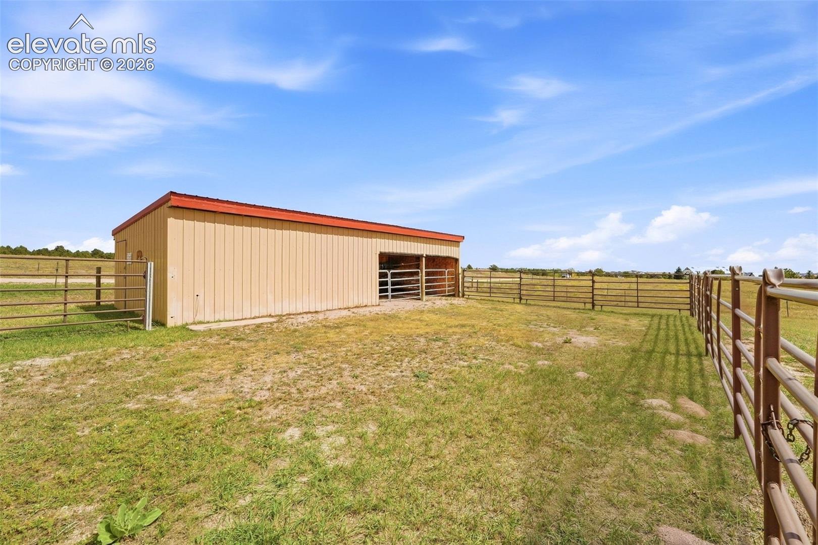 Metal-sided outbuilding with a red roof, multiple fenced enclosures, and a large open area