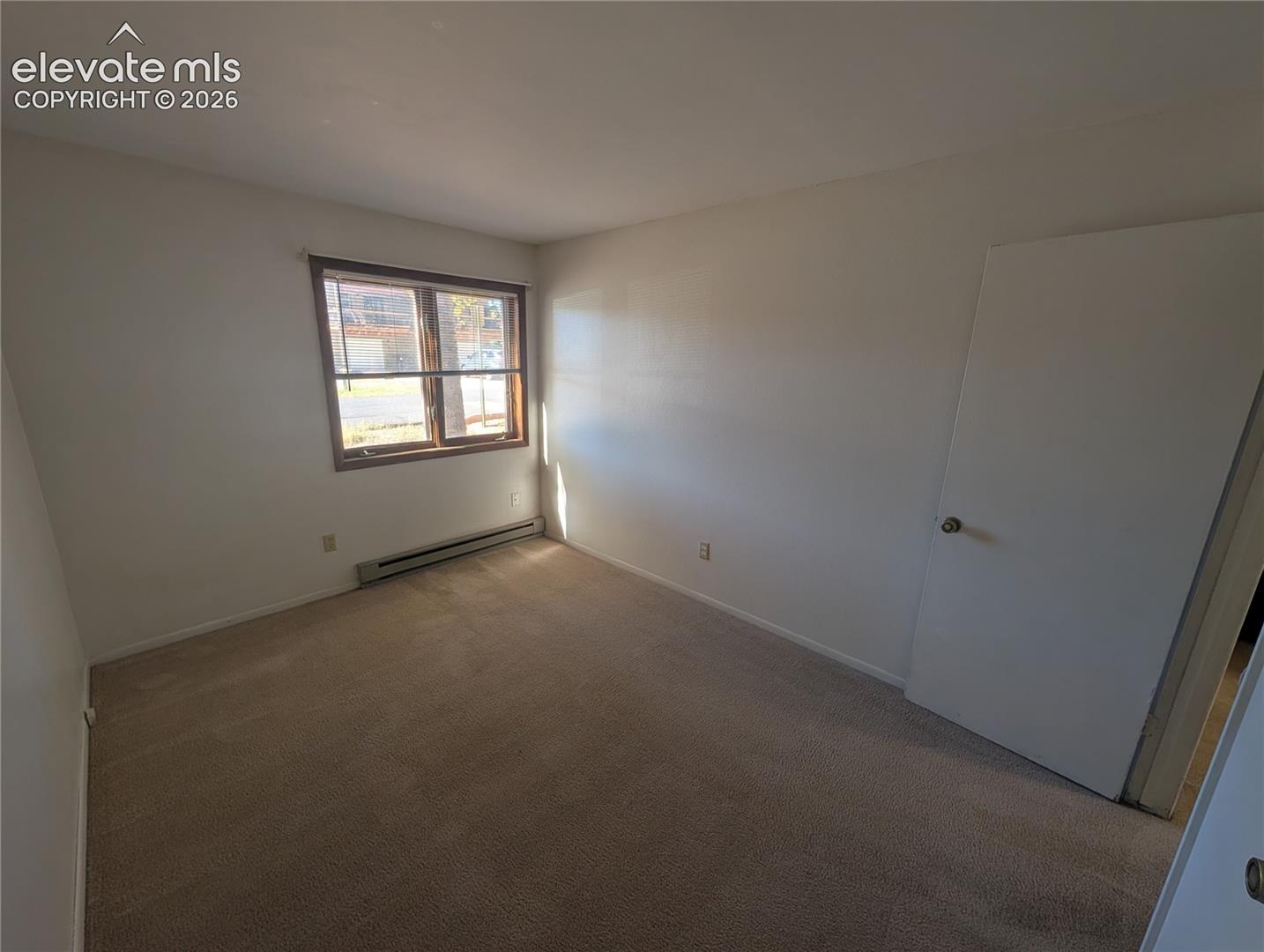 Carpeted flooring, white walls, and a window with wood-finish trim