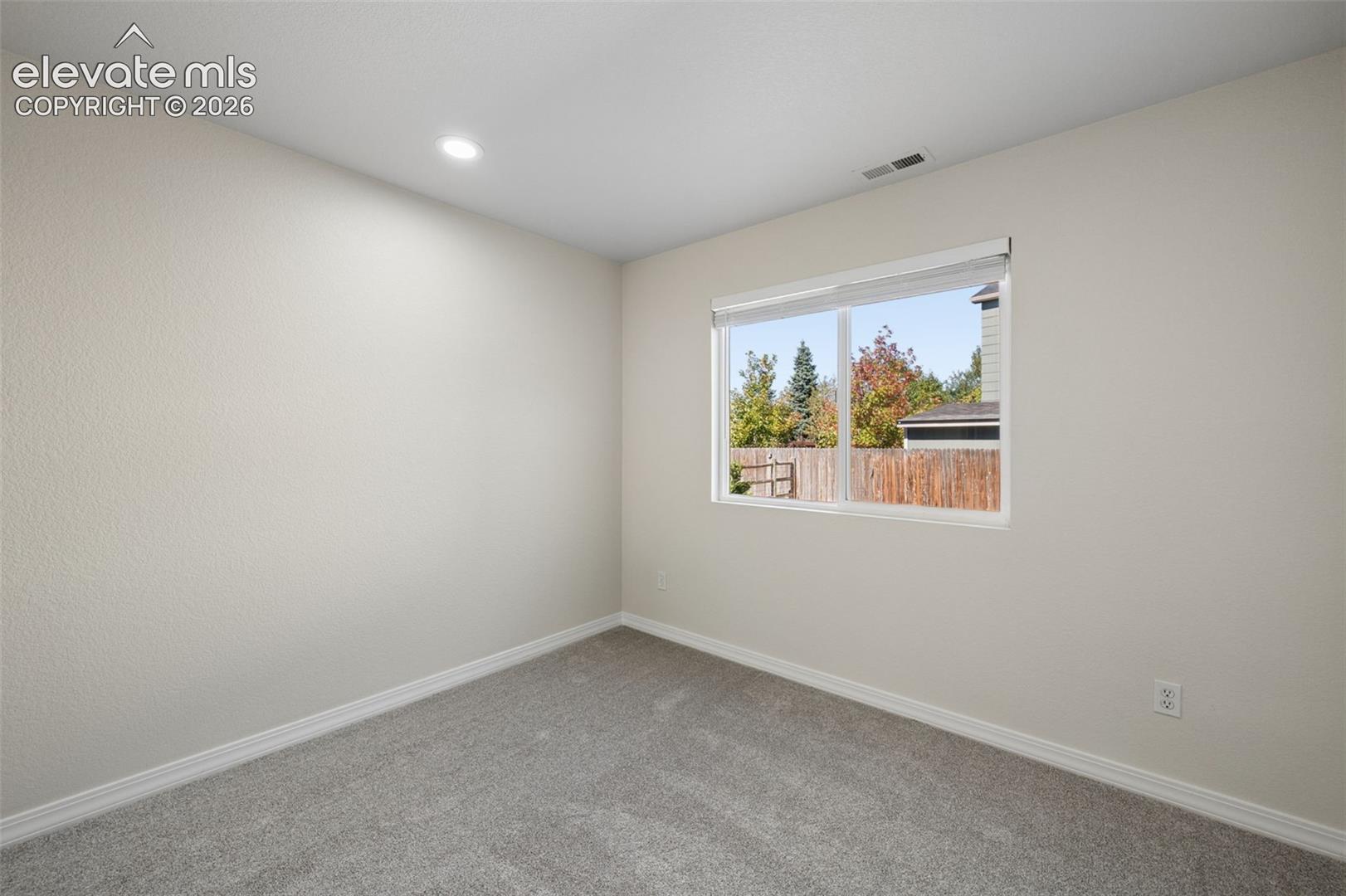 Neutral-toned interior space featuring light-colored wall paint, plush carpeting, recessed lighting, and a single-pane window with blinds