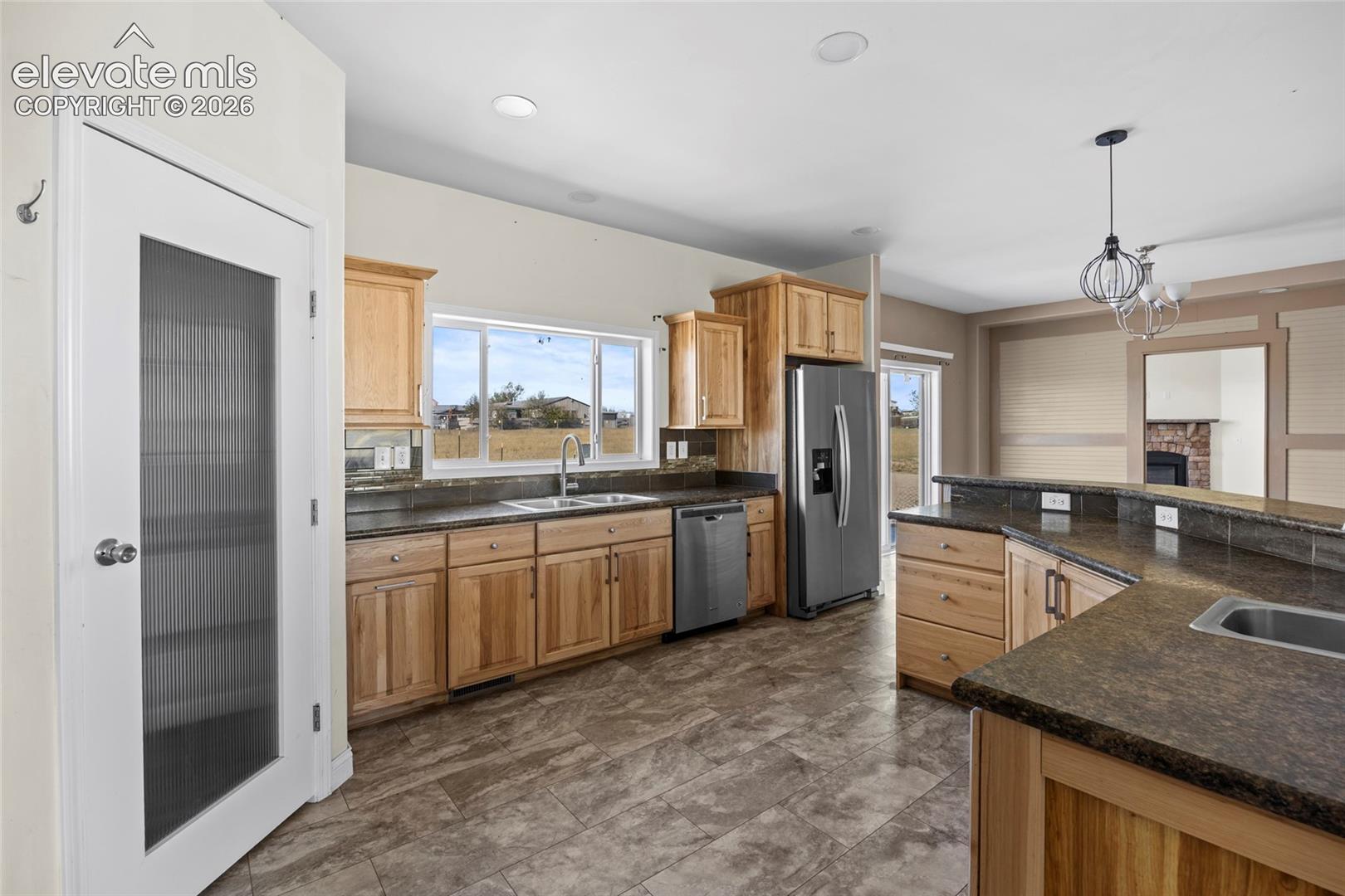 Kitchen featuring natural wood cabinetry, stone-finish countertops, stainless steel appliances, tile flooring, and a frosted glass pantry door