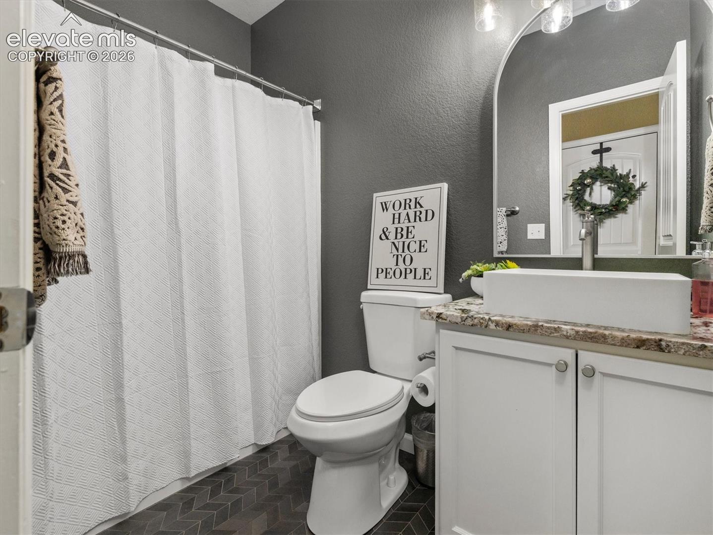 Main level full size bathroom featuring a rectangular vessel sink, white cabinetry, granite countertop, chevron pattern floor tile. Newly remodeled.