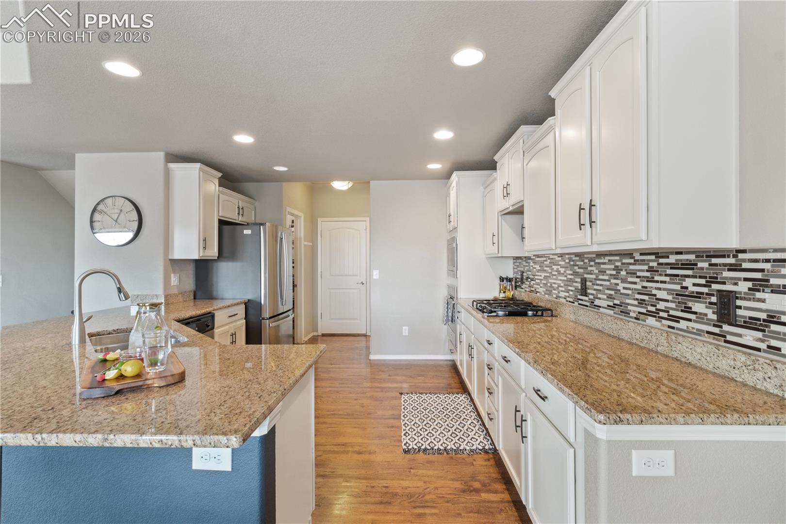 Kitchen with light stone counters, a peninsula, light wood finished floors, white cabinetry, and stainless steel appliances