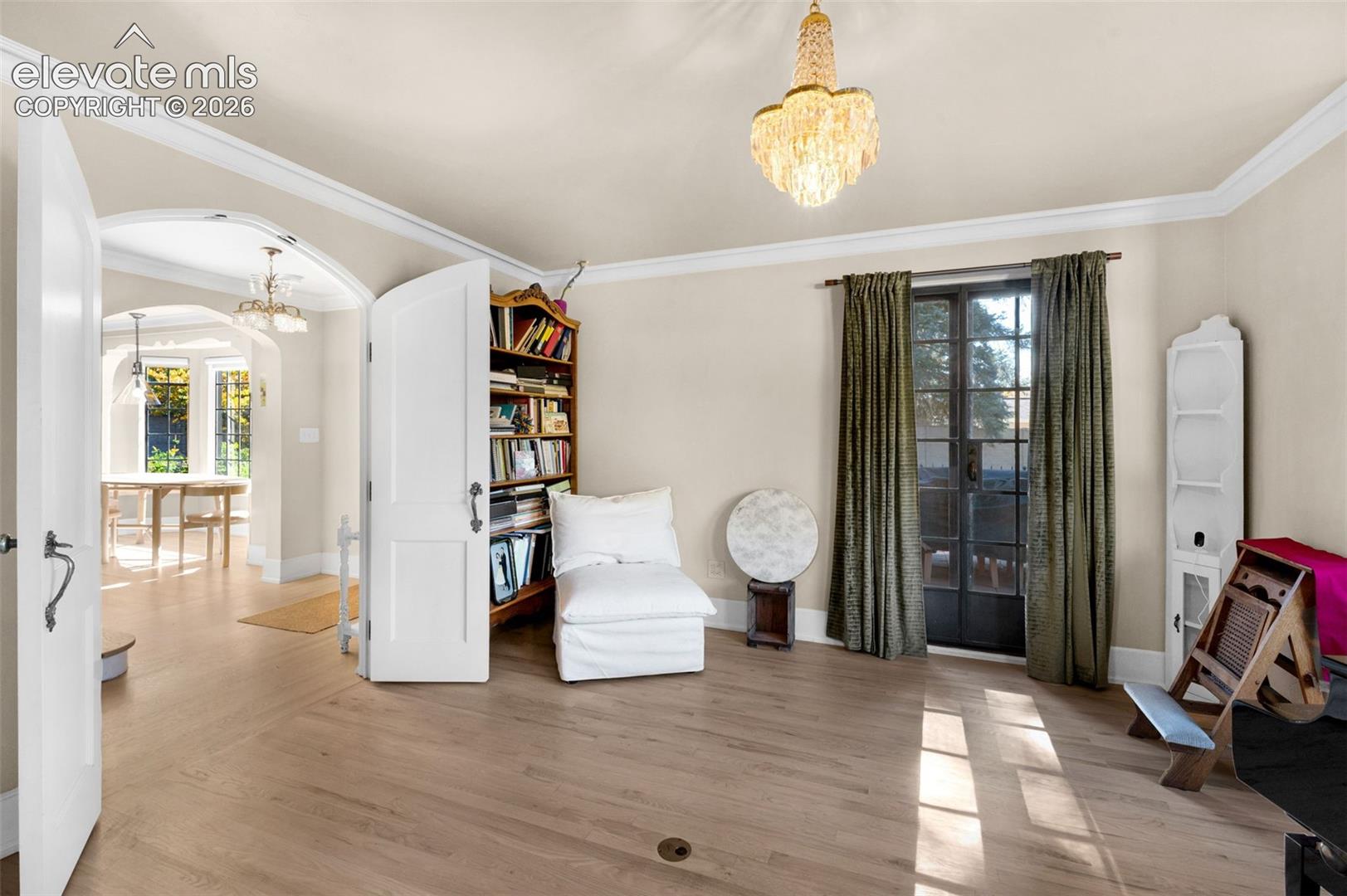 Hardwood flooring, arched doorway, multi-pane glass-panel door, built-in recessed wall shelving, and crystal chandelier fixture