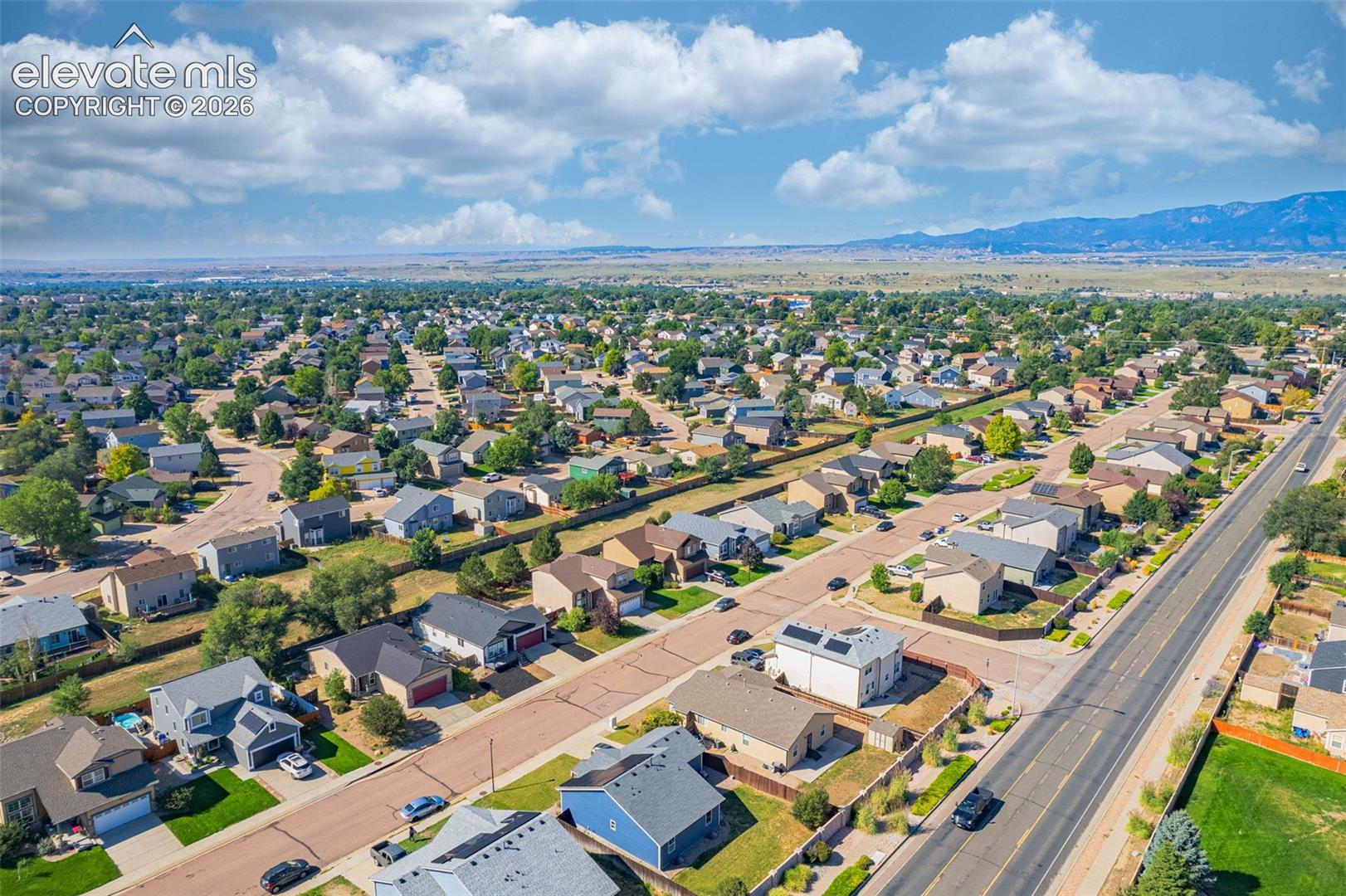 Aerial perspective showcasing a residential neighborhood with established homes, tree-lined streets, and distant mountain scenery