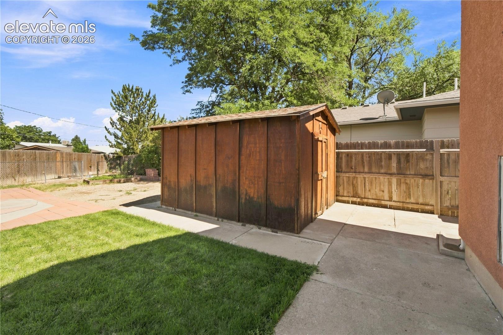 Wood-sided shed, concrete patio, grass lawn, wood fencing, and mature trees