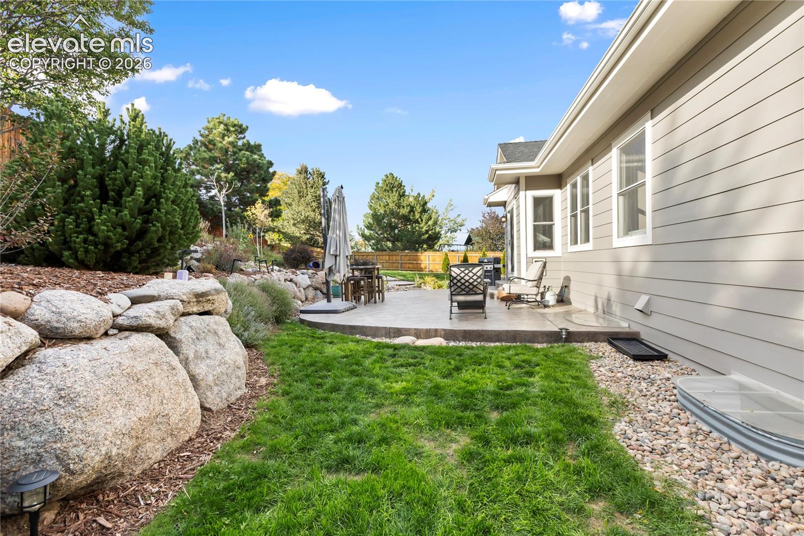 Expansive patio with concrete surfacing, surrounded by a rock retaining wall and established landscaping