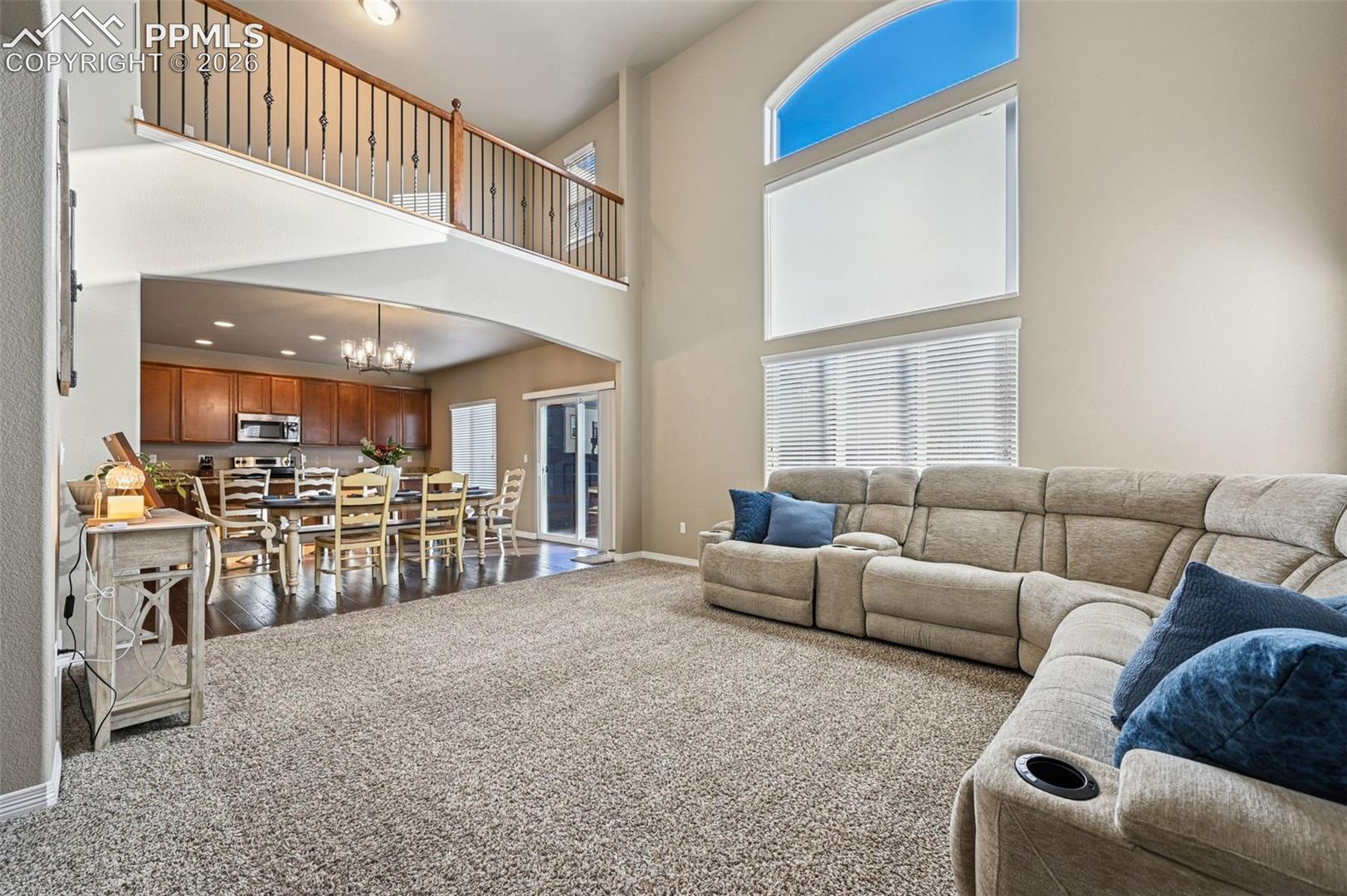 Living area with dark colored carpet, a chandelier, arched walkways, and a high ceiling