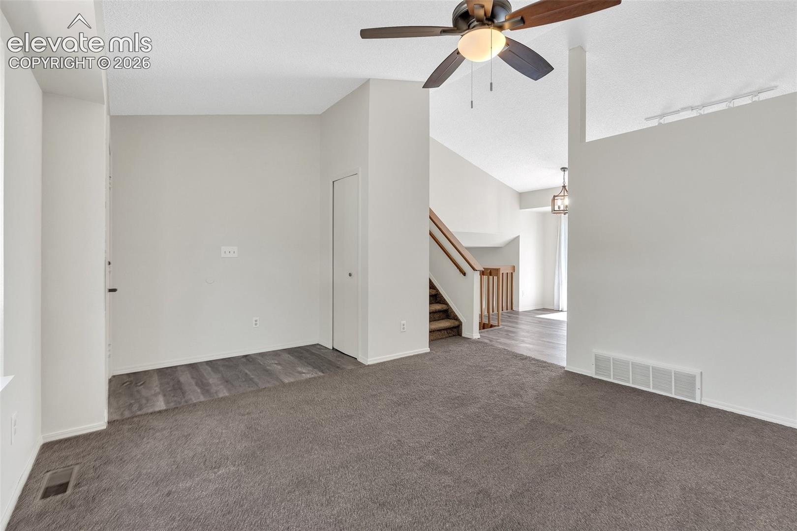 Carpeted living area with a ceiling fan, wood-finish flooring, and a staircase with wood railings