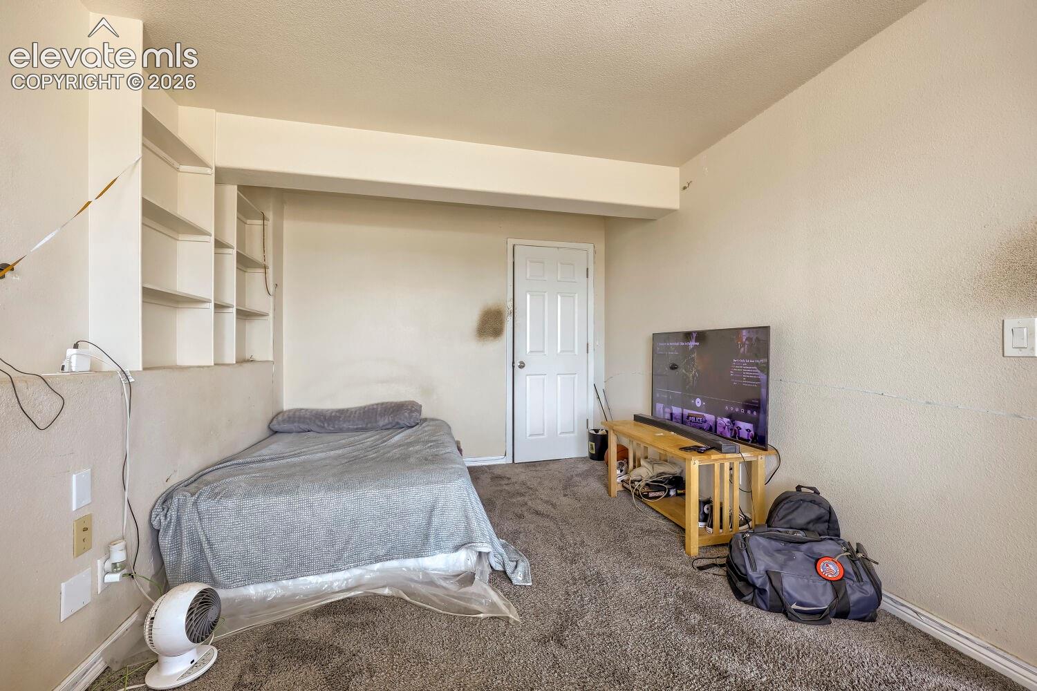 Built-in shelving, white painted interior door, light-colored walls, textured ceiling, and neutral carpet