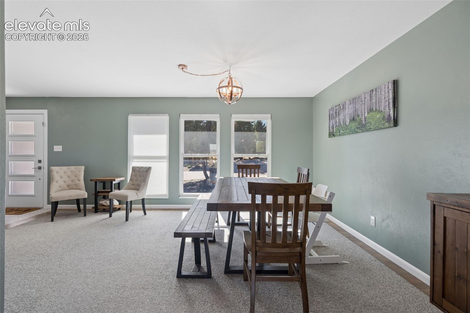 Neutral-toned interior space featuring three large windows, a spherical metal-finish pendant light, and a front entry door with four glass panels