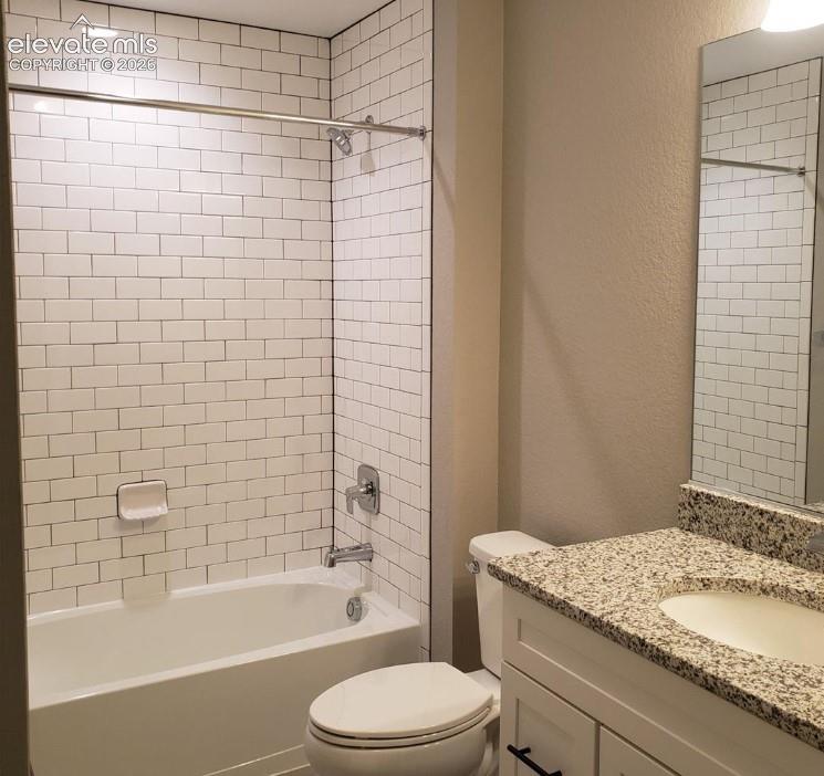 Bathroom featuring a tub-shower combination with white subway tile surround, vanity with stone-finish countertop, undermount sink, and wall-mounted mirror