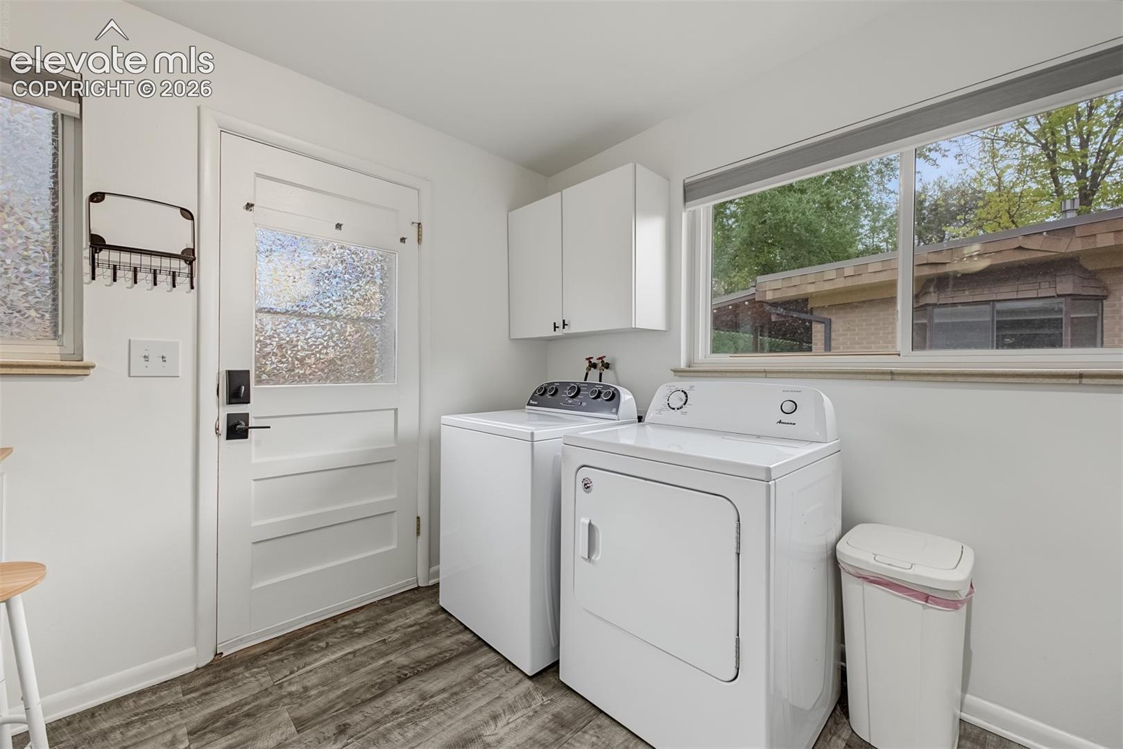 Laundry room featuring wood-finish flooring, white wall-mounted cabinetry, a large window, and an exterior door with a textured glass pane