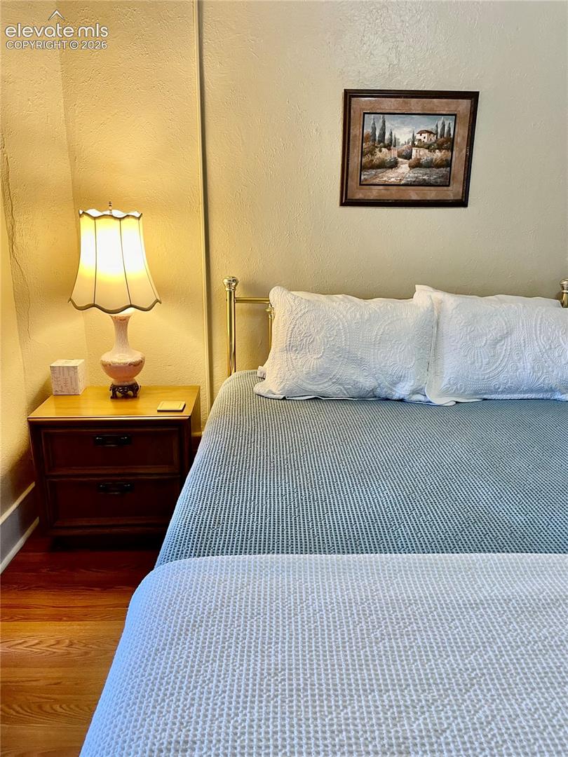 Inviting bedroom featuring warm ambient lighting from a traditional table lamp, hardwood flooring, brass-finished bed frame, and soft textiles