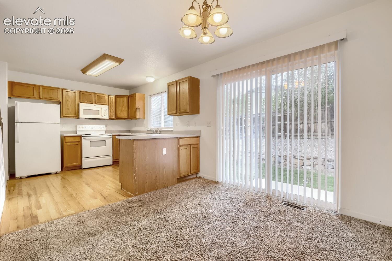 Kitchen featuring wood cabinetry, white appliances, a peninsula, wood-finish flooring, and sliding glass doors