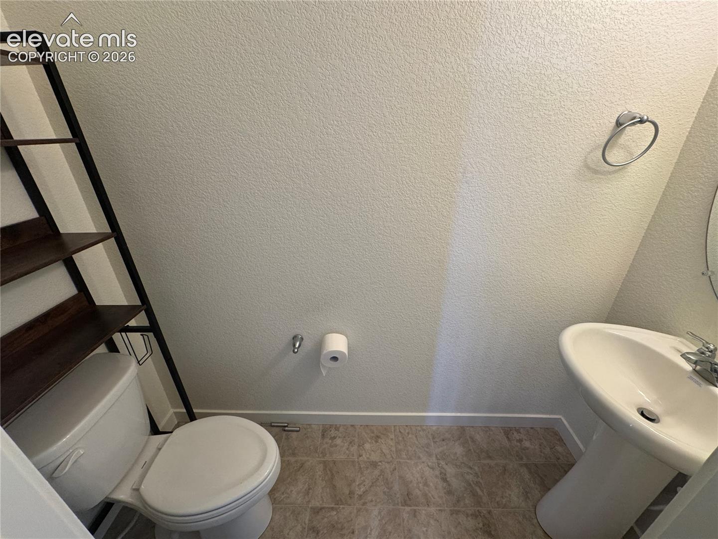 Pedestal sink with polished chrome faucet, textured wall finish, and tiled flooring