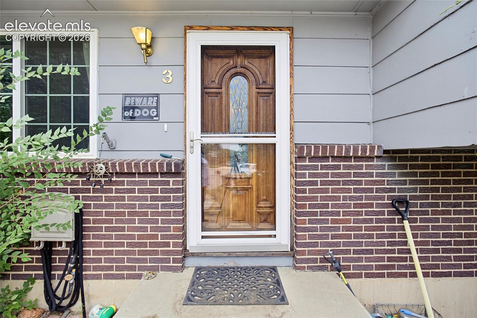 Entryway featuring a wood-finish door with frosted glass detailing, a clear storm door, and a brick facade