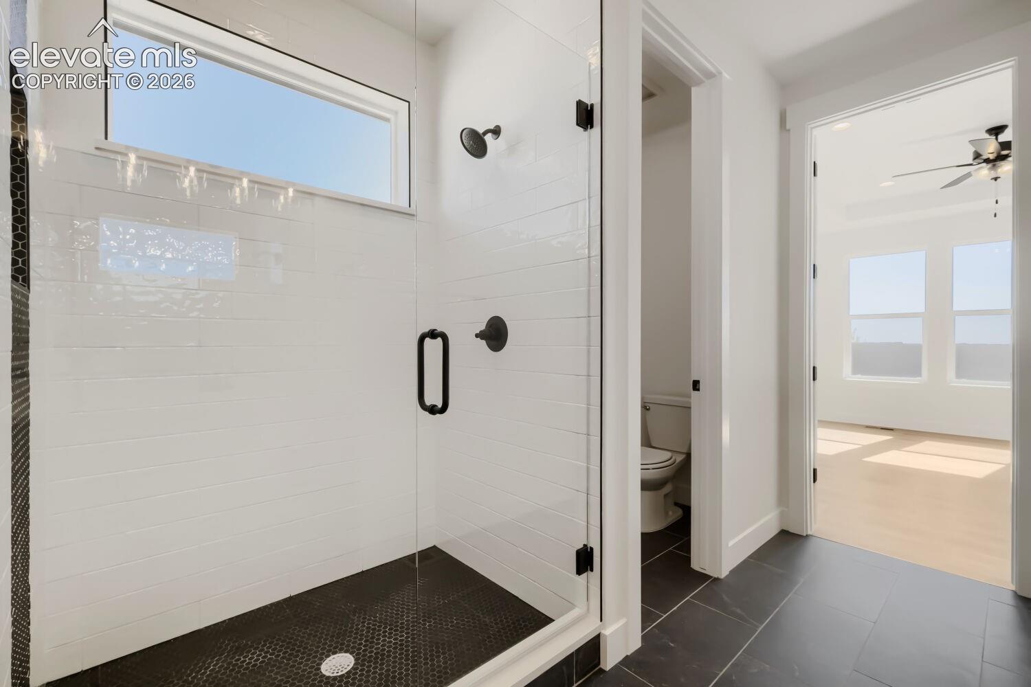 Primary Bathroom featuring a frameless glass-enclosed shower with subway tile surround, matte black hardware and showerhead, dark tile flooring with integrated drain, and direct access to an adjacent bedroom space