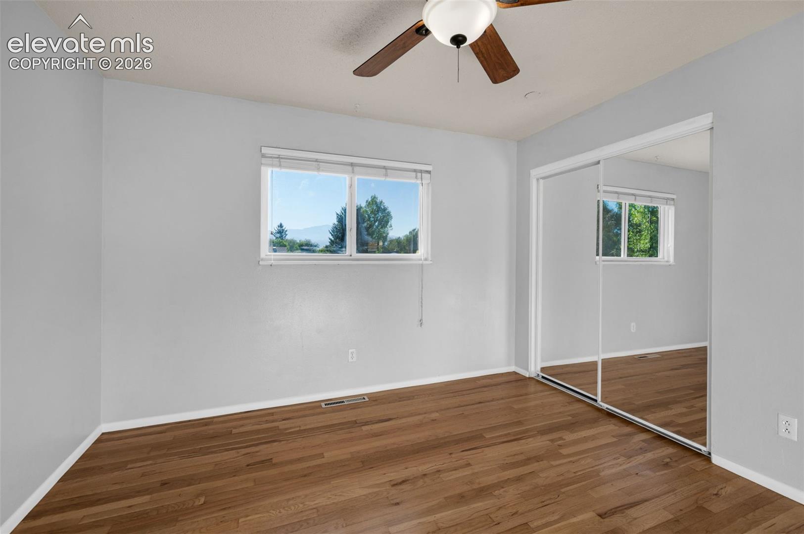 bedroom featuring wood-finish flooring, a ceiling fan, sliding mirrored closet doors