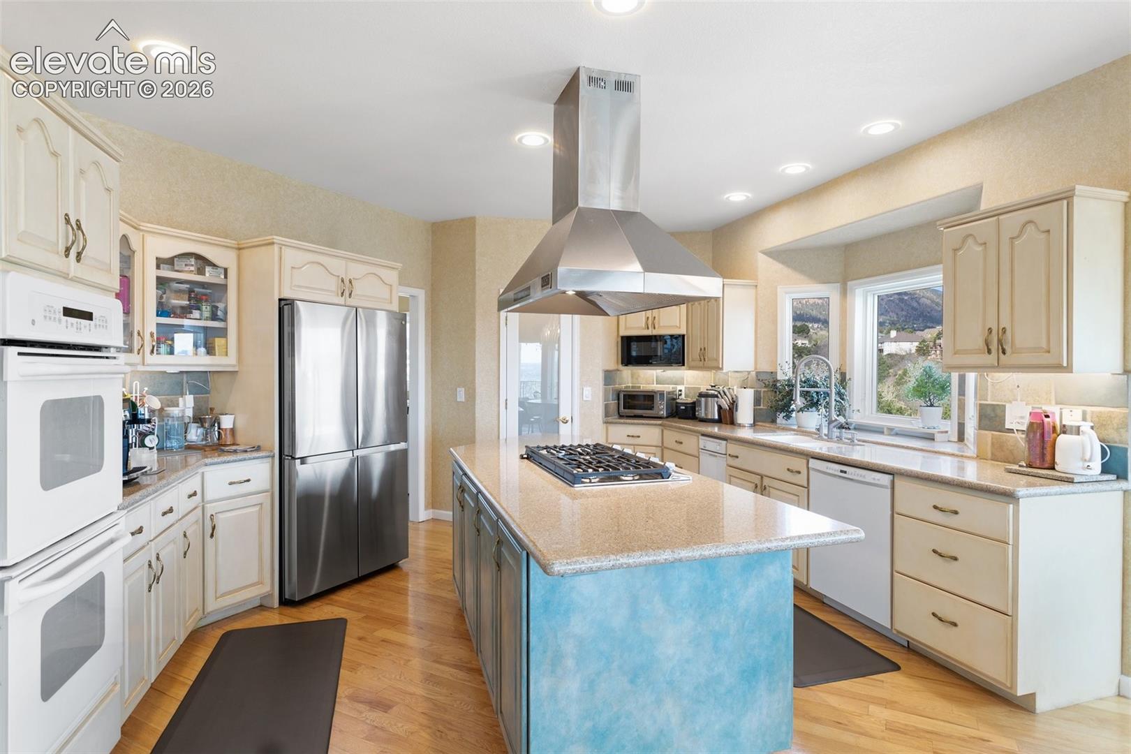 Spacious kitchen featuring an expansive central island with a built-in cooktop, stainless steel appliances, abundant cabinetry, wood-finish flooring, and recessed lighting