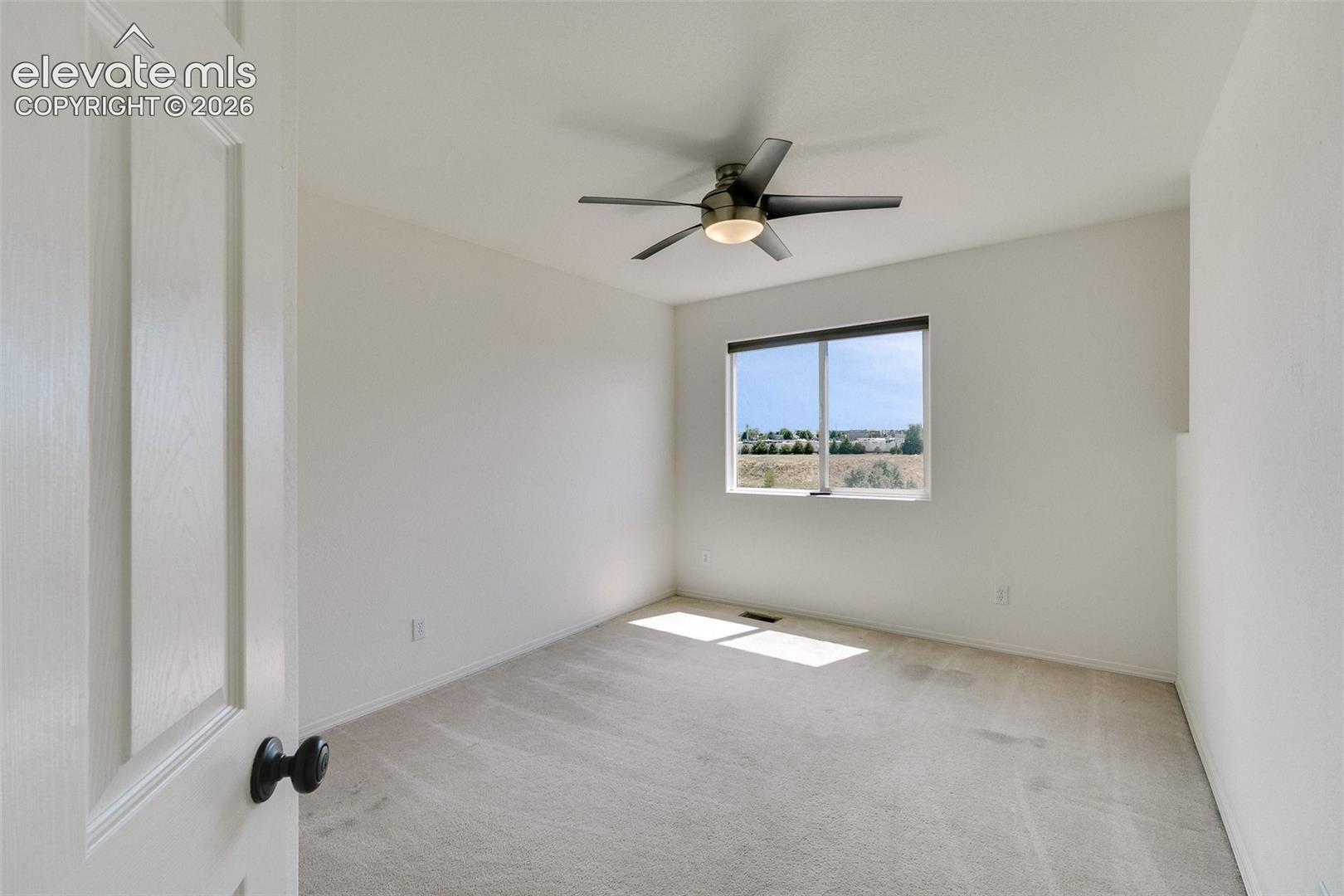 Carpeted flooring, a window with a roller shade, and a ceiling fan with integrated lighting