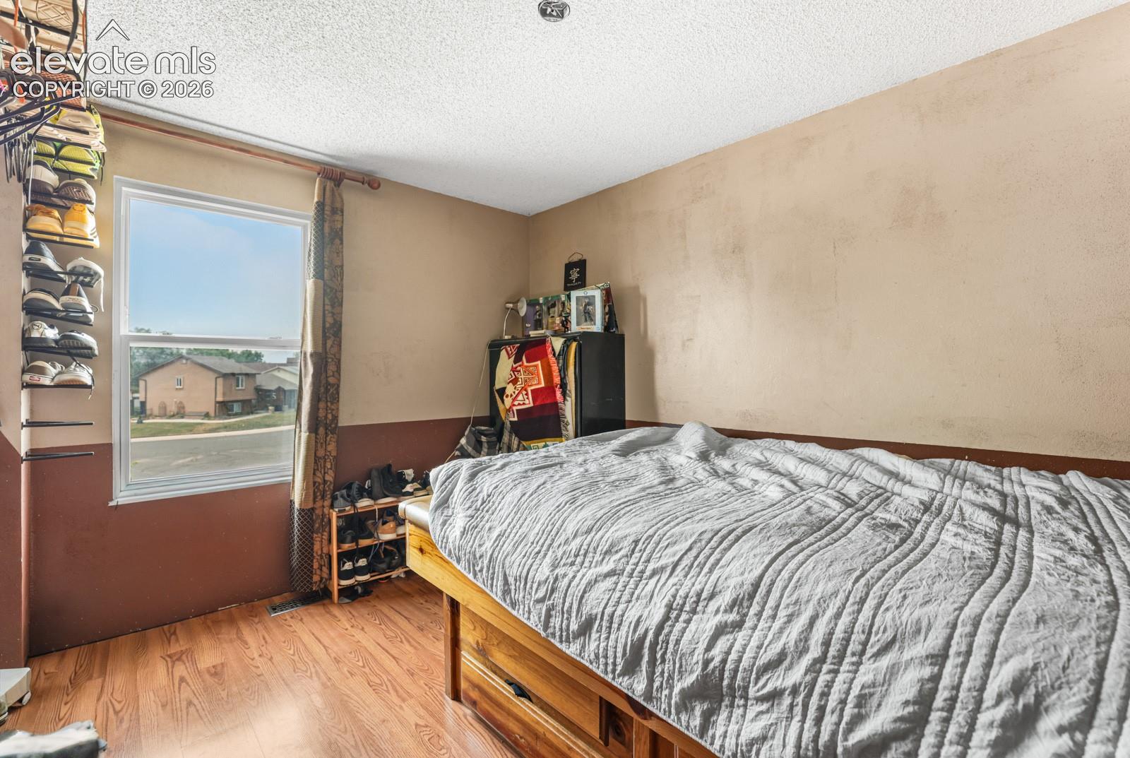 Bedroom with wood-finish flooring, two-tone wall treatment, and a window with a curtain rod
