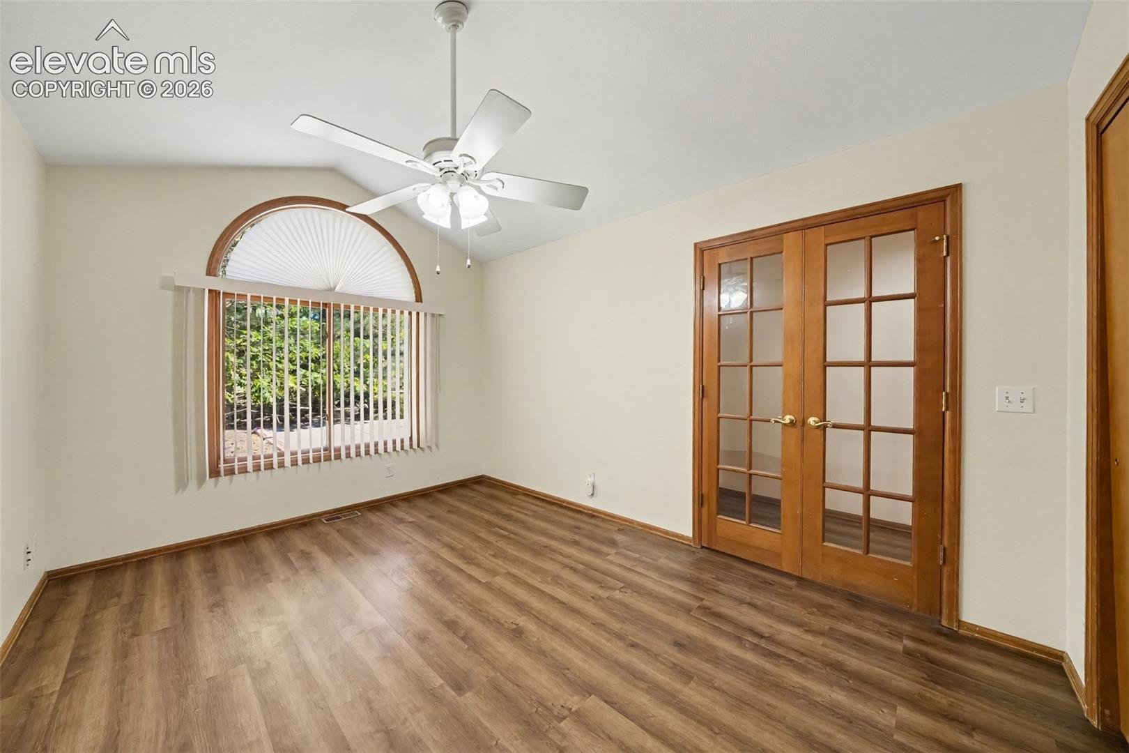 Vaulted ceiling with a ceiling fan, LVP flooring, French doors, and a large arched window